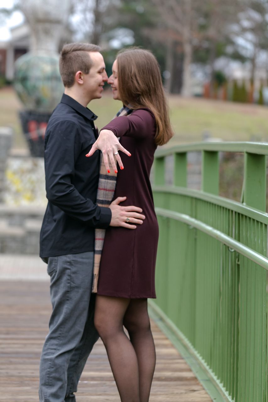 Couple on green bridge — Couple facing each other on a green bridge, she in a burgundy dress with red nails, he in a black shirt.