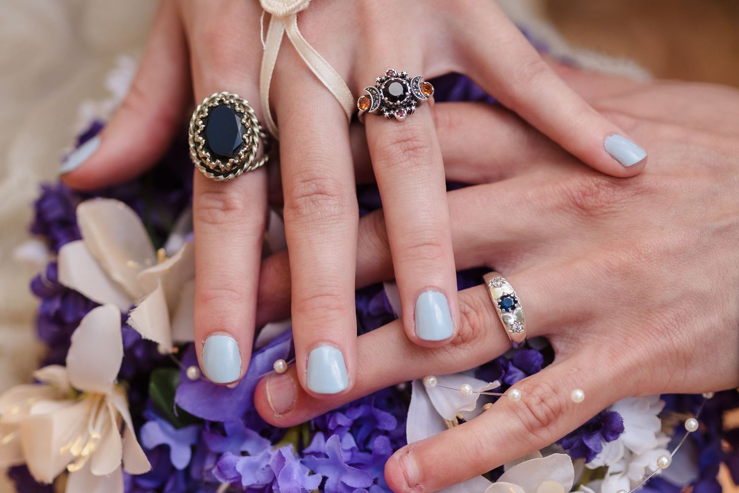 Wedding rings on bouquet — Romantic wedding detail of two hands with vintage rings resting on purple and white floral bouquet.