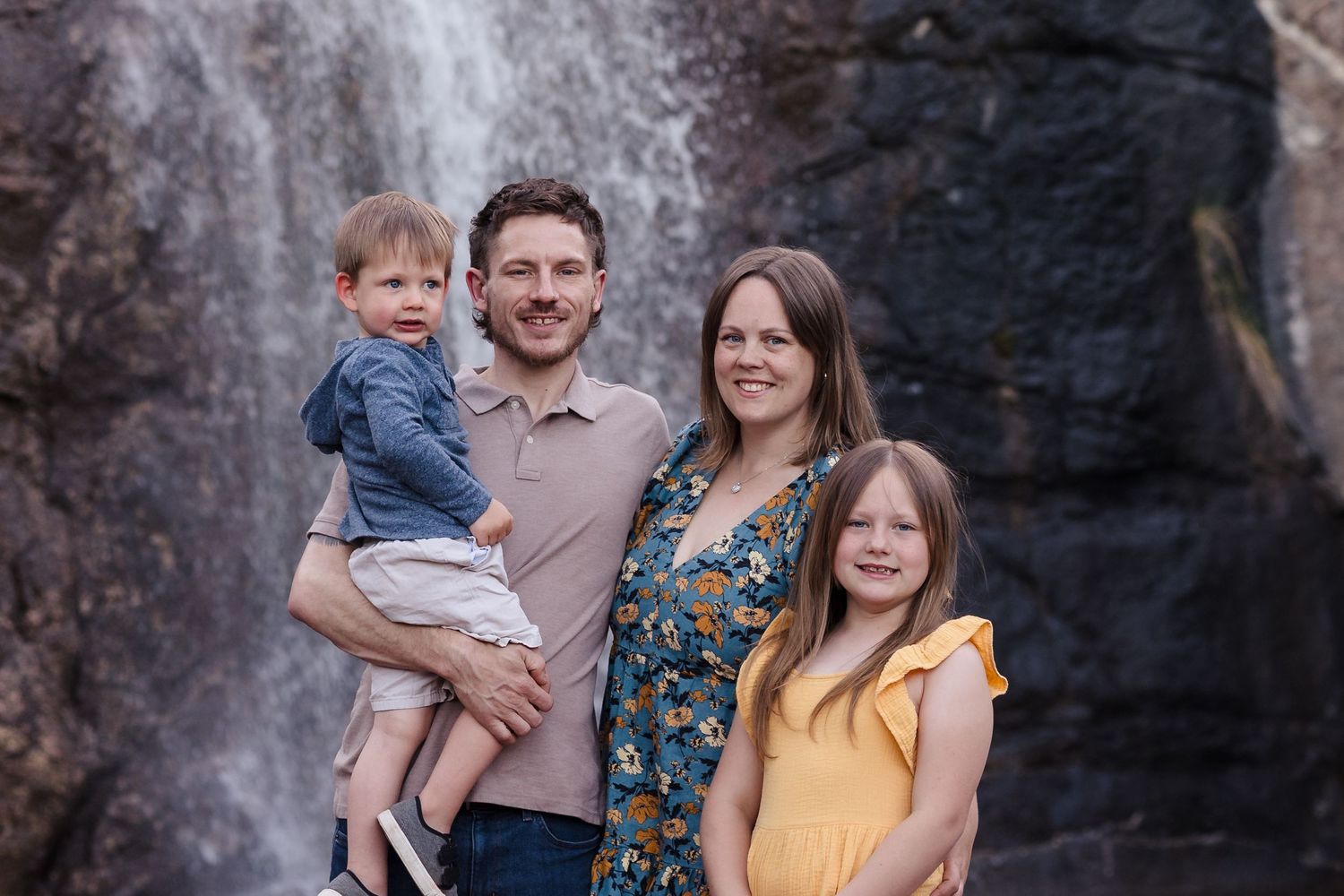 Family of four waterfall — Family of four smiling together in front of a scenic waterfall during an outdoor session.