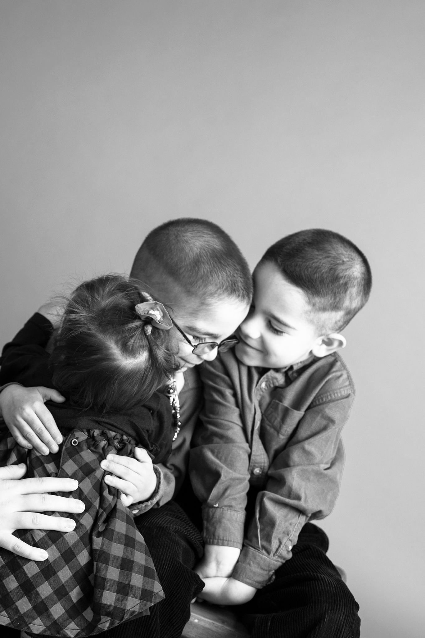 Three kids black and white hug — Black and white portrait of three young children hugging and smiling closely together.