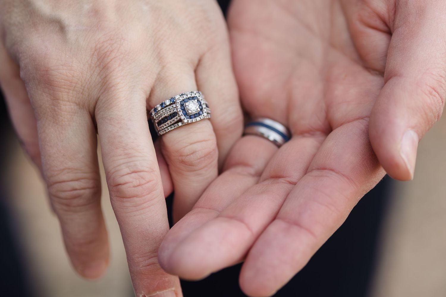 Close-up of two hands displaying matching black diamond and silver wedding ring set.