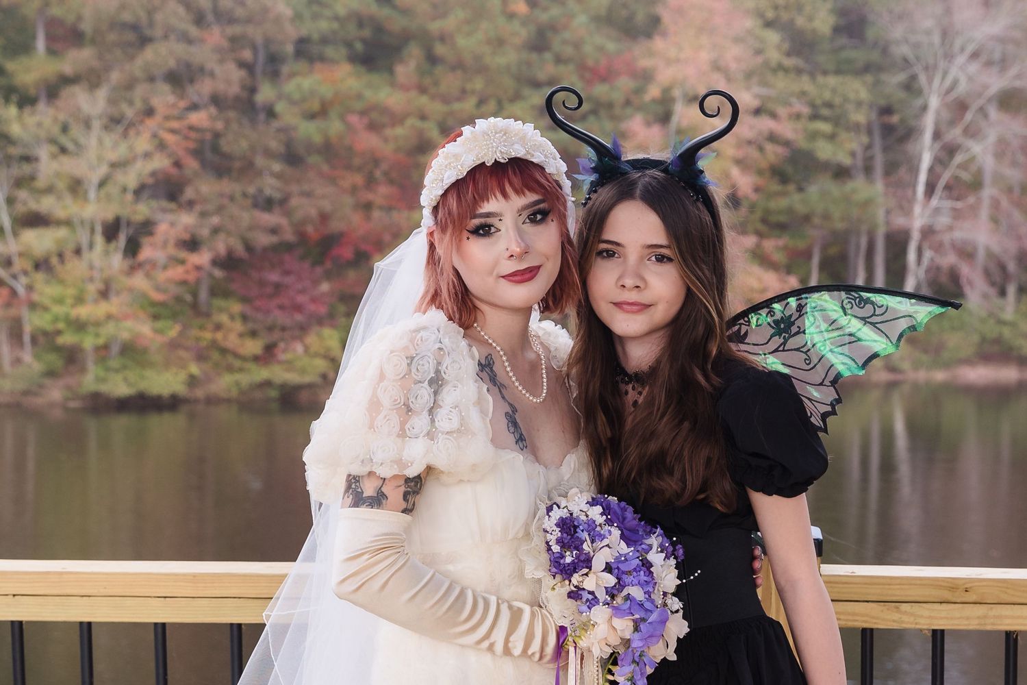 Two women in fantasy costumes pose together at lakeside autumn wedding celebration.