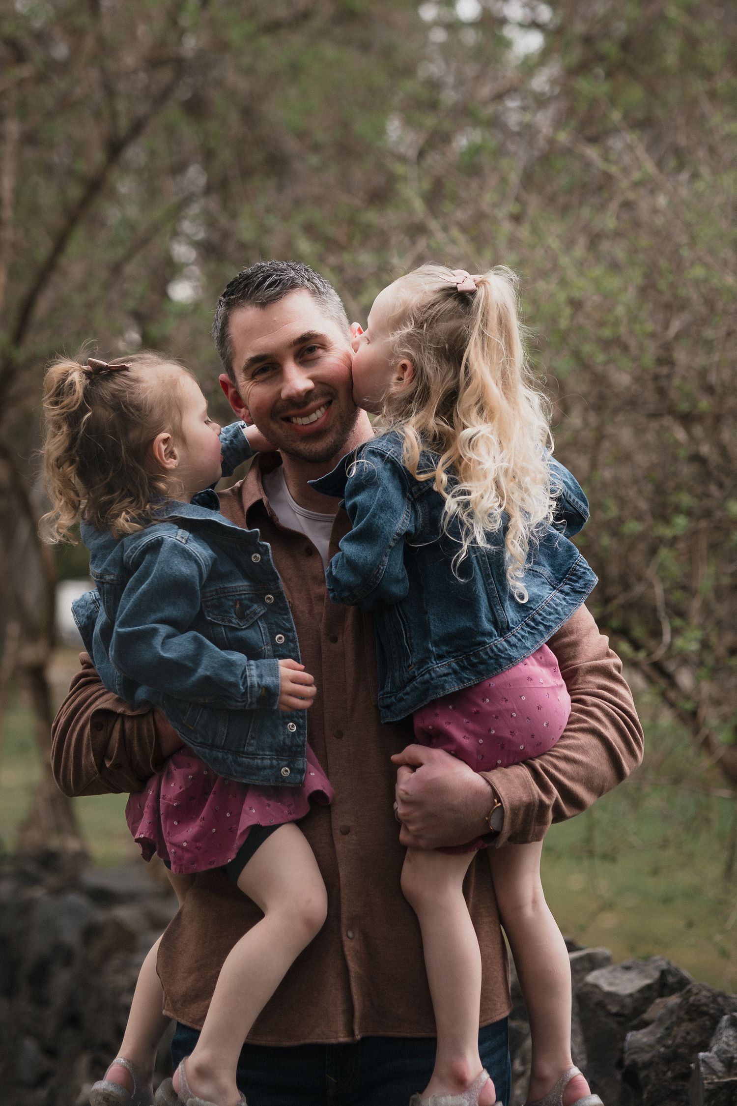 Dad holding two girls — Smiling father holding his two little girls in denim jackets and pink dresses during an outdoor session.