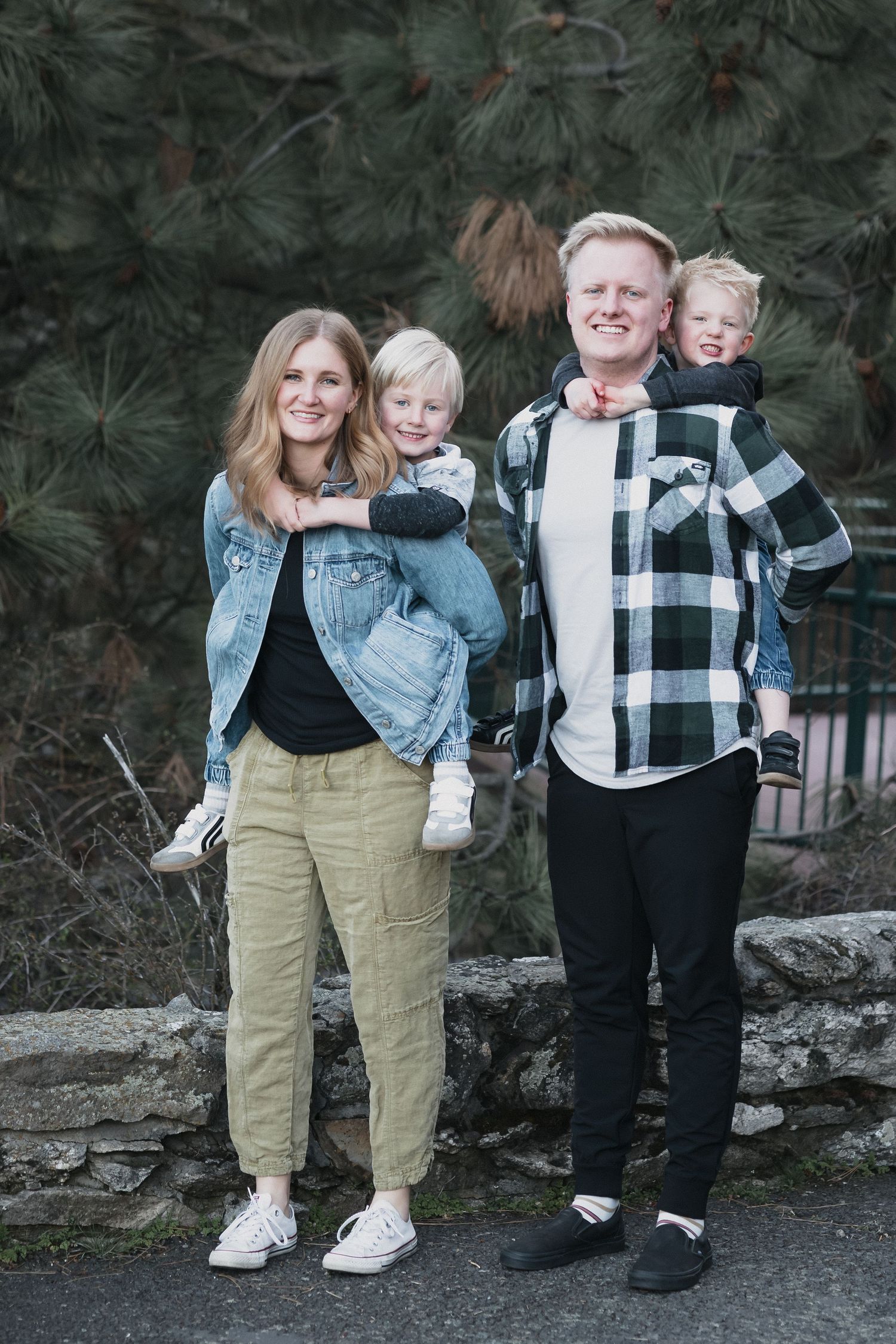 Young family pine trees — Young family of four posing outdoors with tall pine trees in the background.