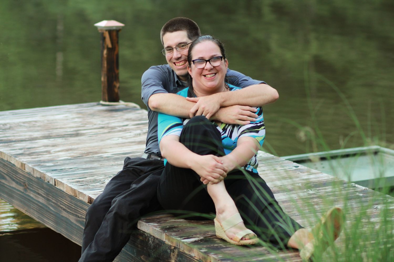 Couple on dock by lake — Couple sitting on a wooden dock by a lake, smiling and embracing during a peaceful outdoor session.