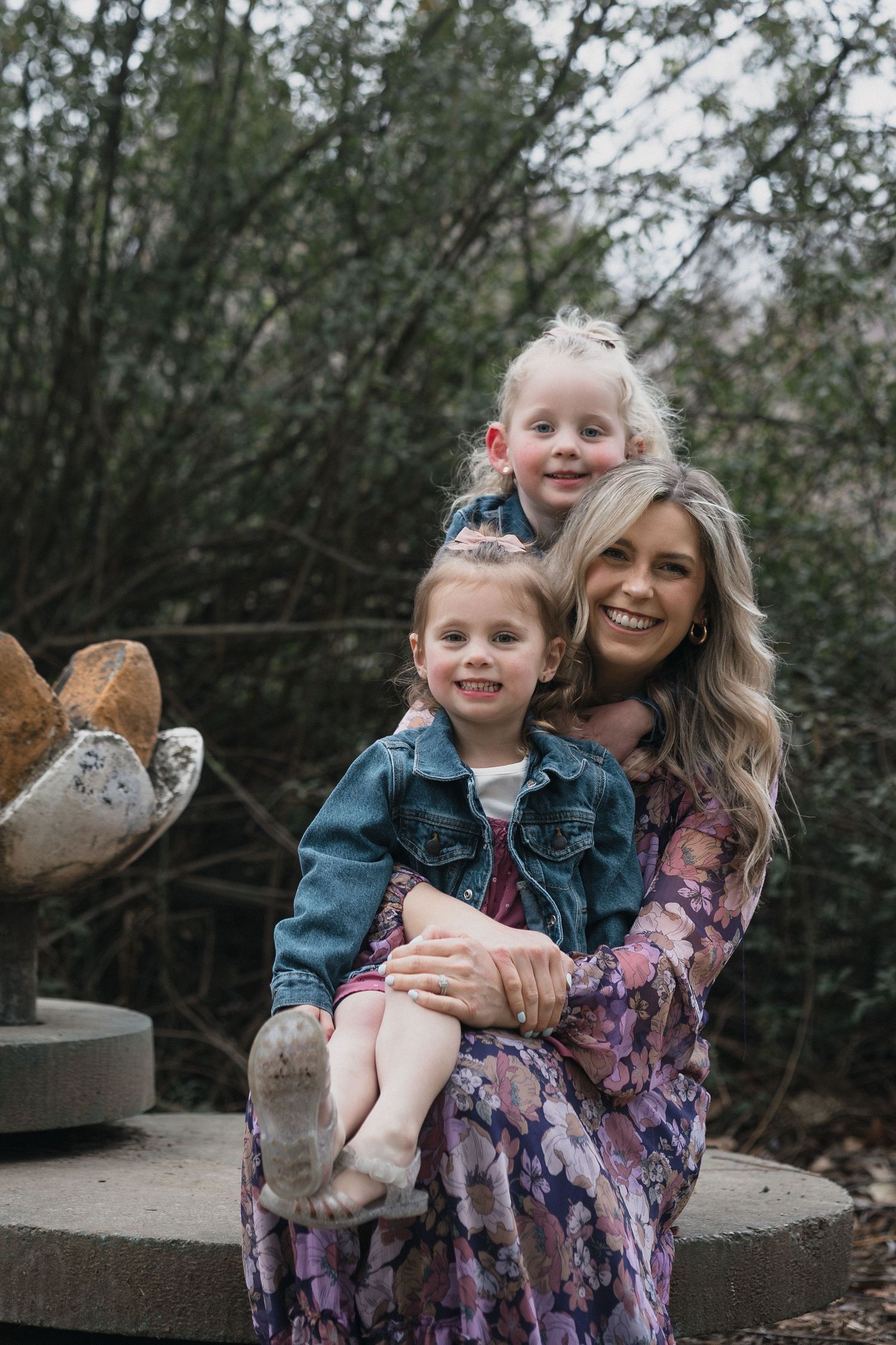 Mom holding two daughters — Smiling mother in a floral dress holding her two young daughters in a garden setting.