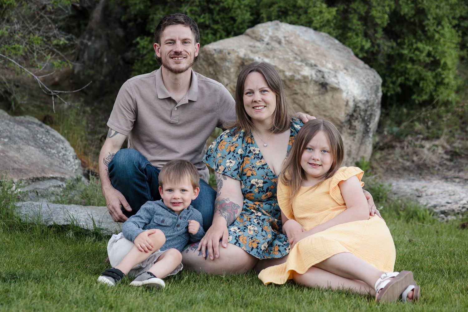 Family of four by boulders — Happy family of four sitting on green grass near large boulders in a park.