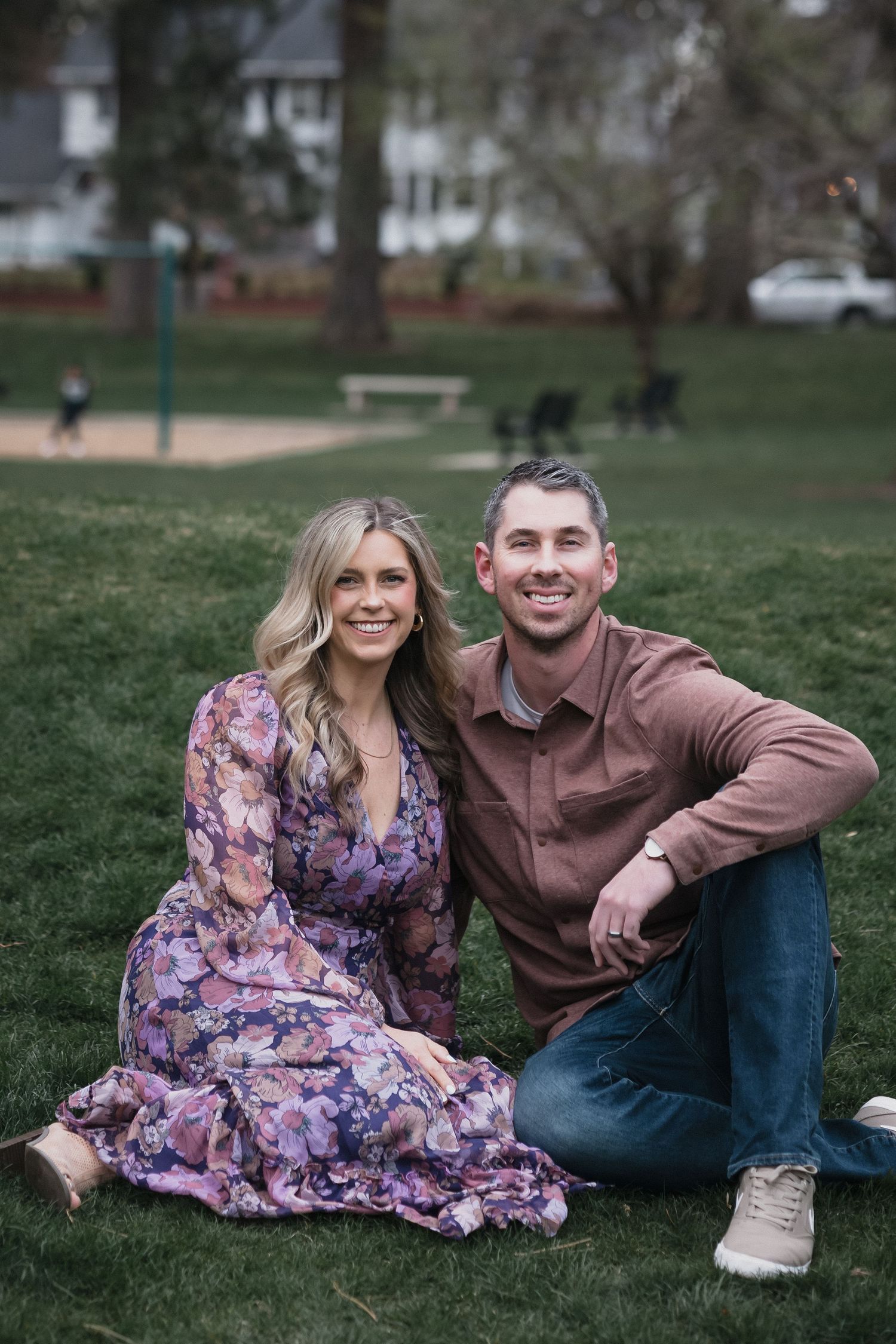 Couple sitting on grass — Smiling couple sitting together on green grass in a park, the woman in a floral dress.