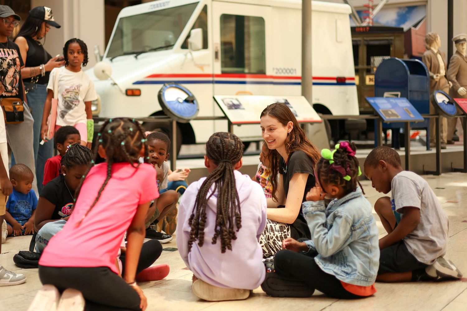 A woman sits on the ground engaging with a group of children at a museum.