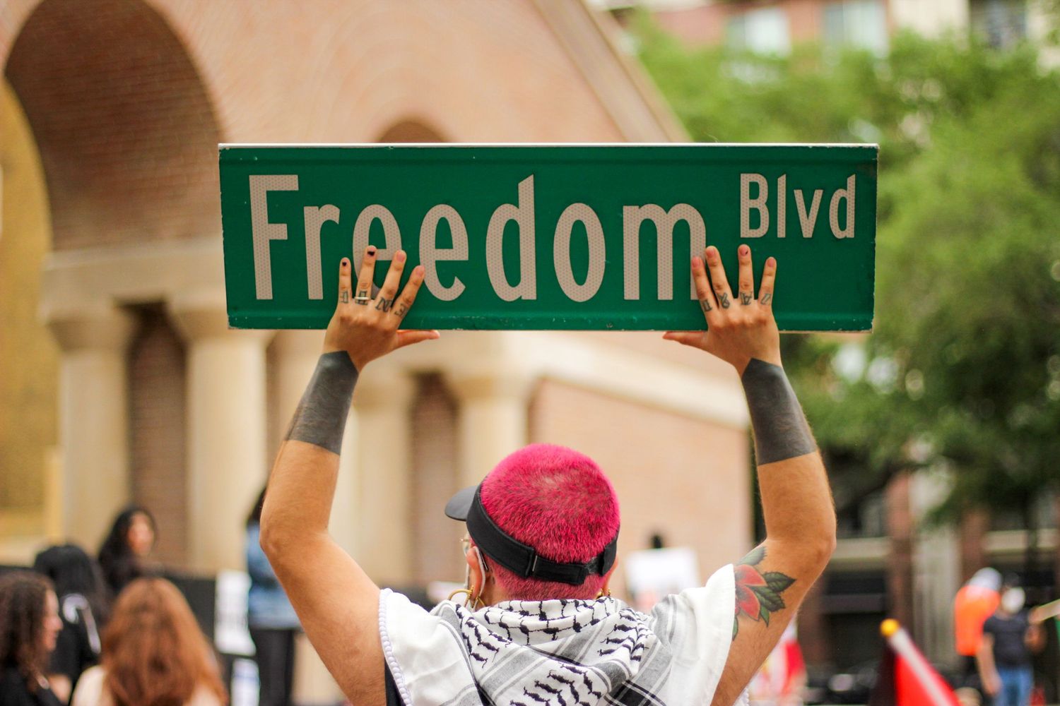 Person holds a Freedom Blvd street sign overhead at an outdoor demonstration.