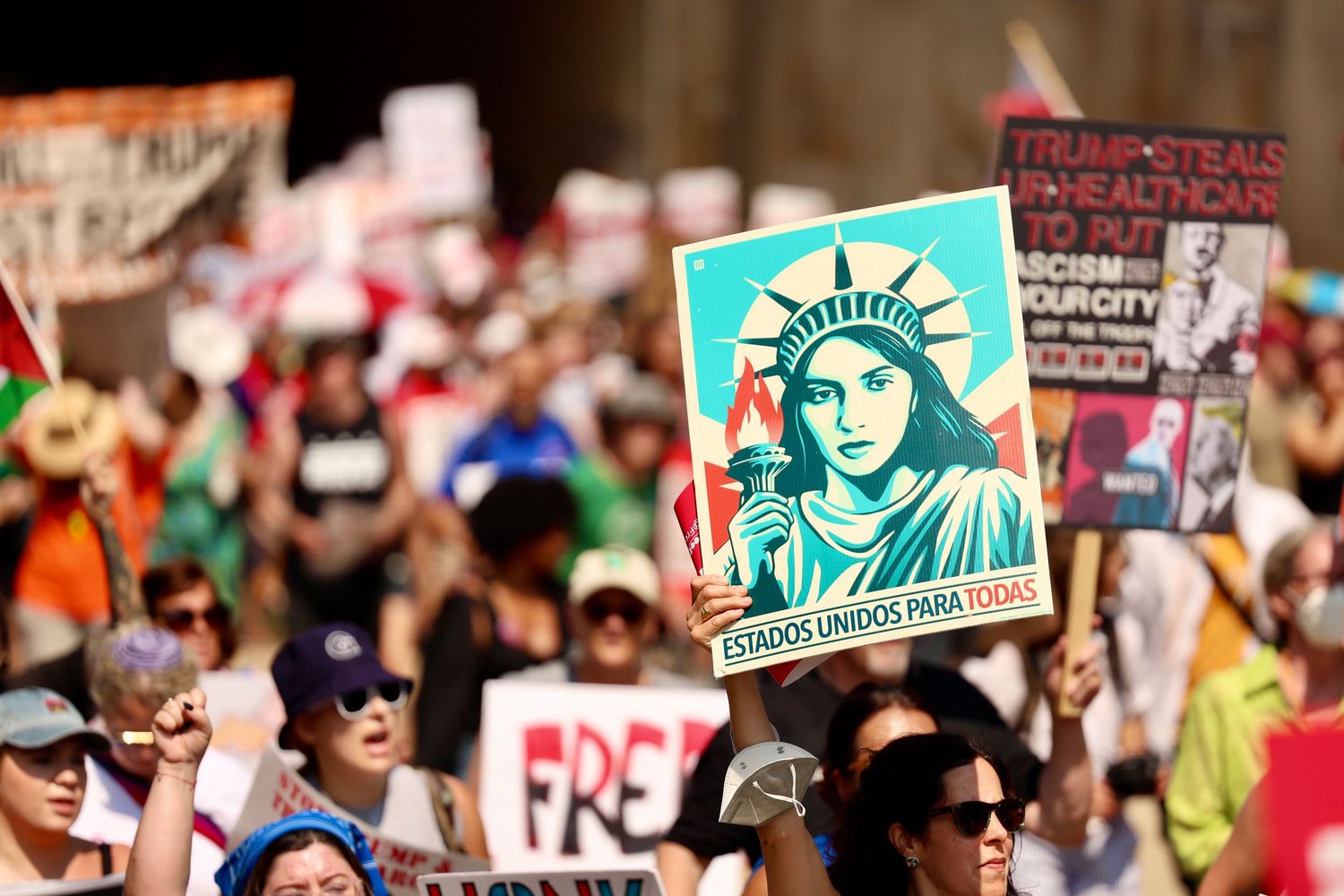 Protesters march holding signs including a Statue of Liberty poster reading Estados Unidos Para Todos at a political rally.
