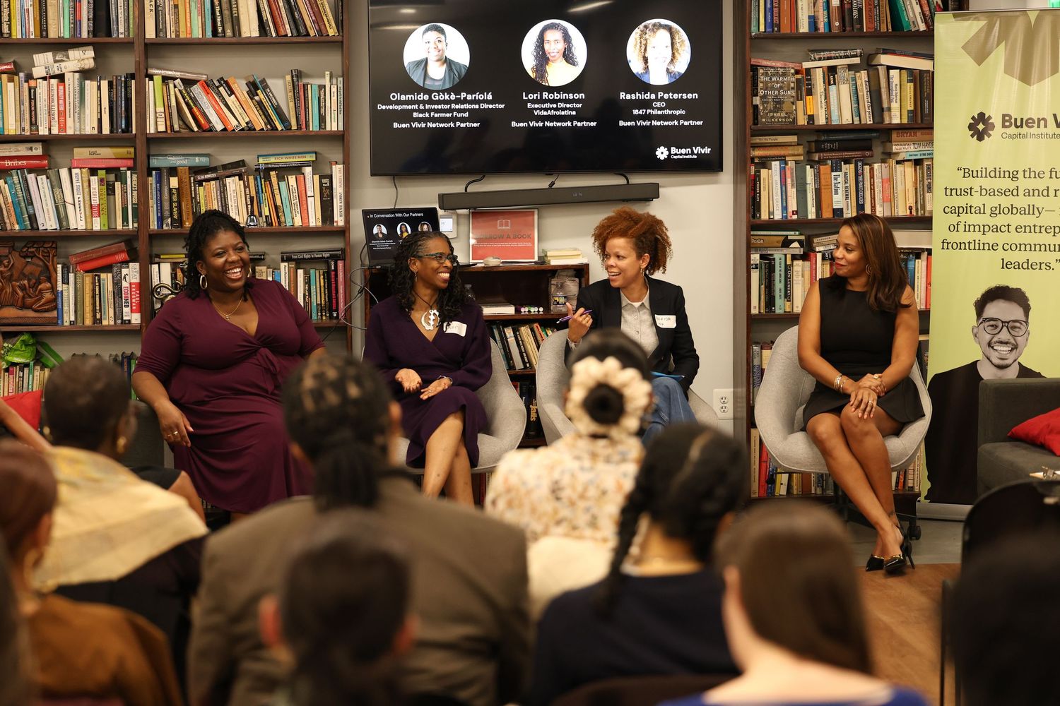 Four women participate in a panel discussion at an event in front of an audience.
