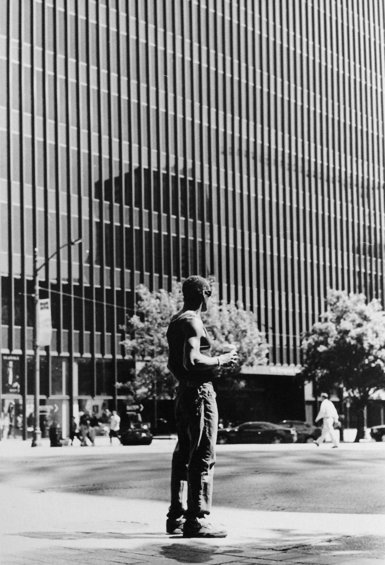 Black and white photo of a man standing on a city street corner with a large modern office building behind him.
