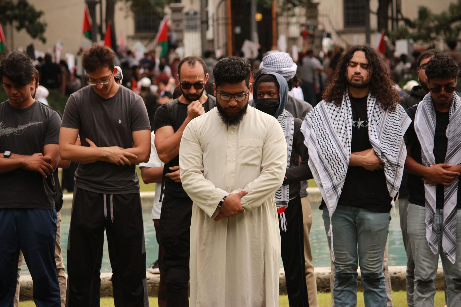 Group of men standing in prayer outdoors at a rally, wearing traditional and casual attire.