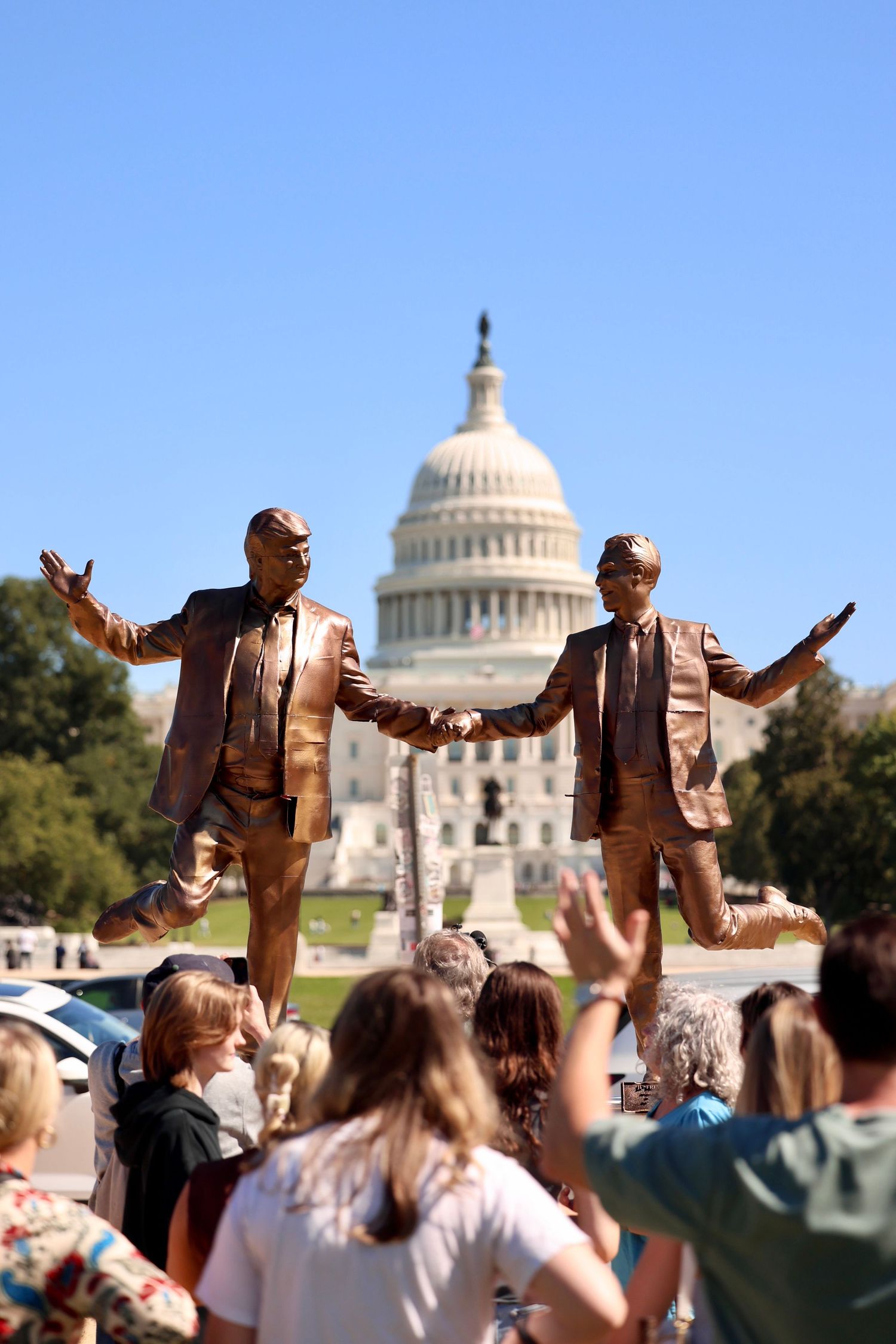 Bronze statues of two men shaking hands displayed in front of the US Capitol building.