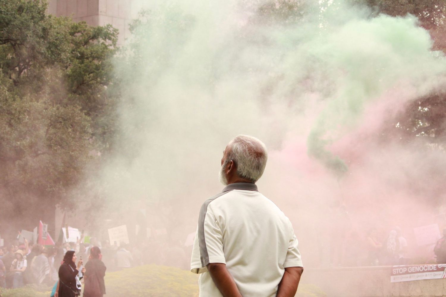 Elderly man watches colorful powder smoke clouds fill the air at an outdoor event.