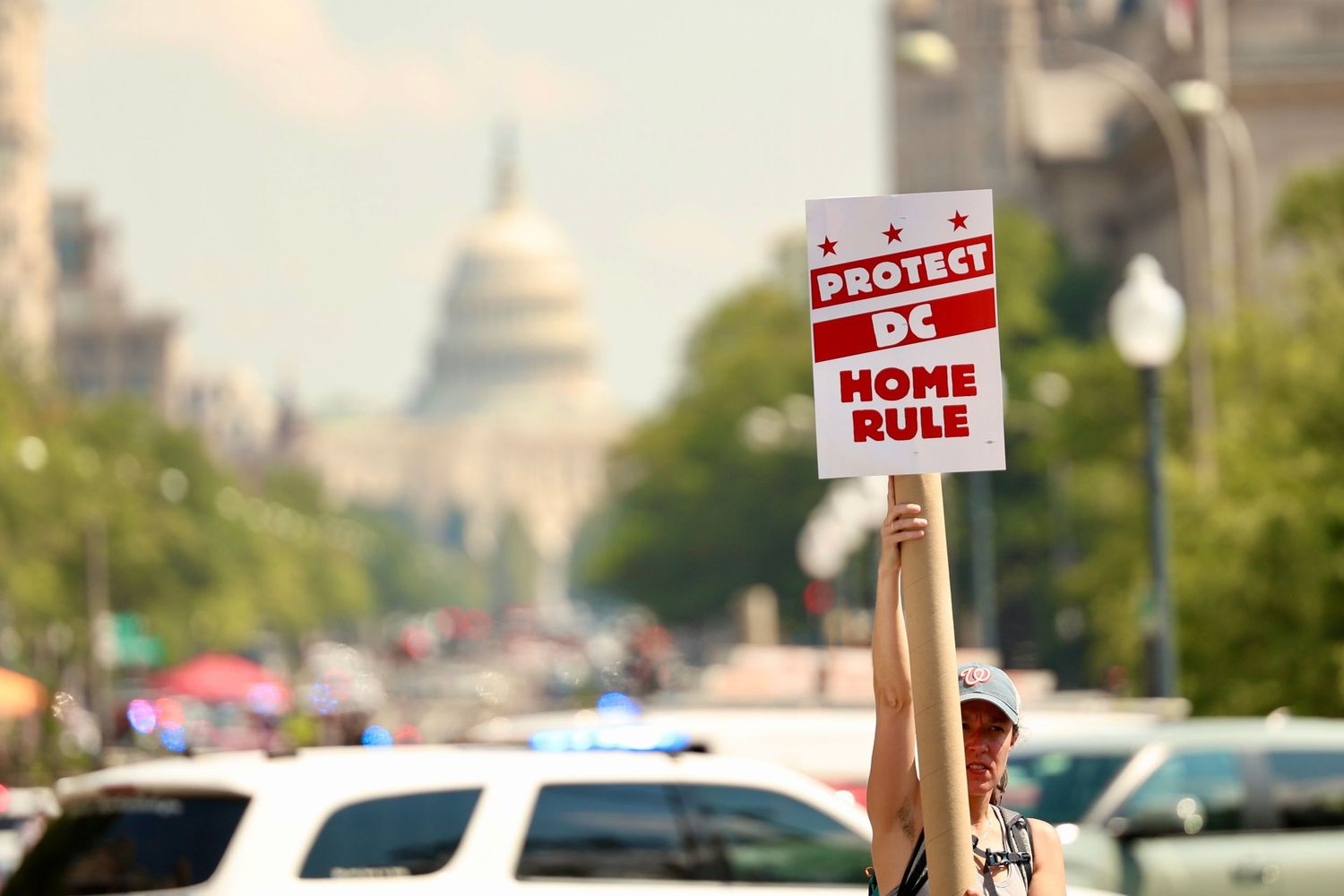 A protester raises a Protect DC Home Rule sign near Pennsylvania Avenue with the US Capitol behind.