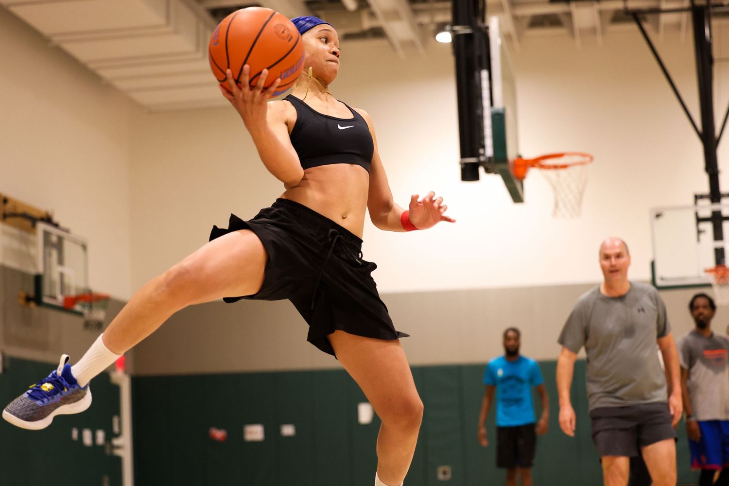 A female basketball player leaps mid-air preparing to shoot during an indoor gym practice session.