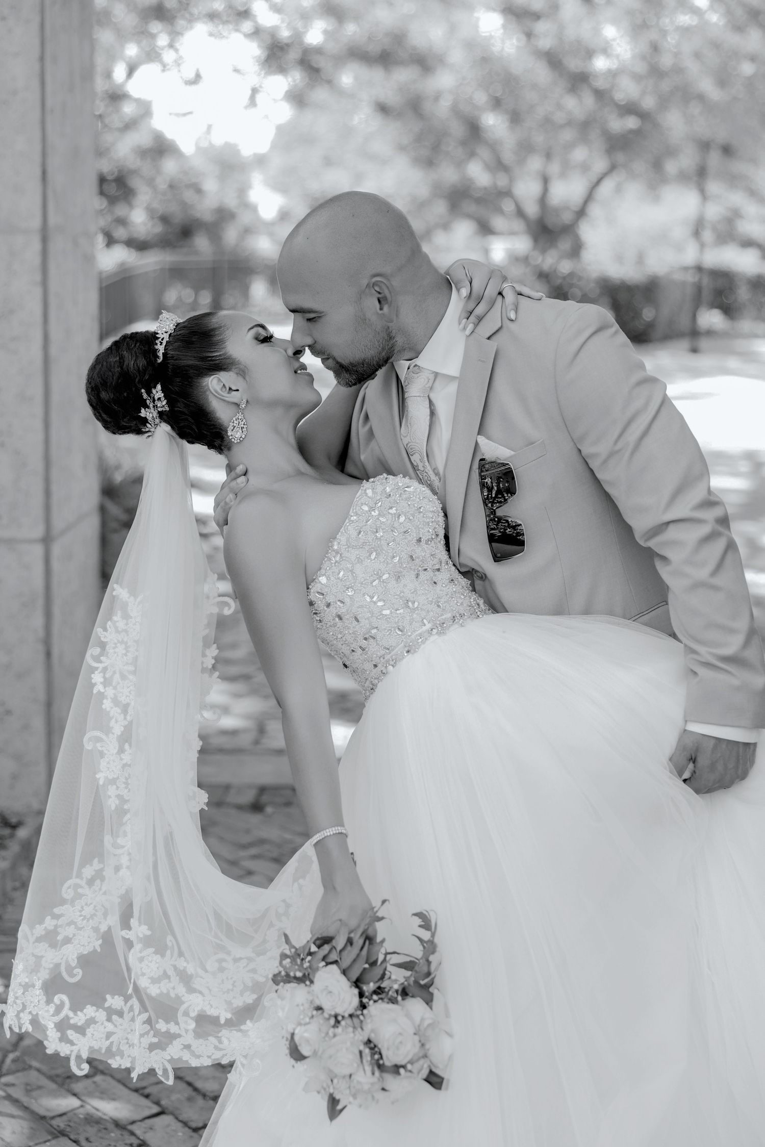 Black and white portrait of a groom dipping and kissing his bride during an outdoor wedding