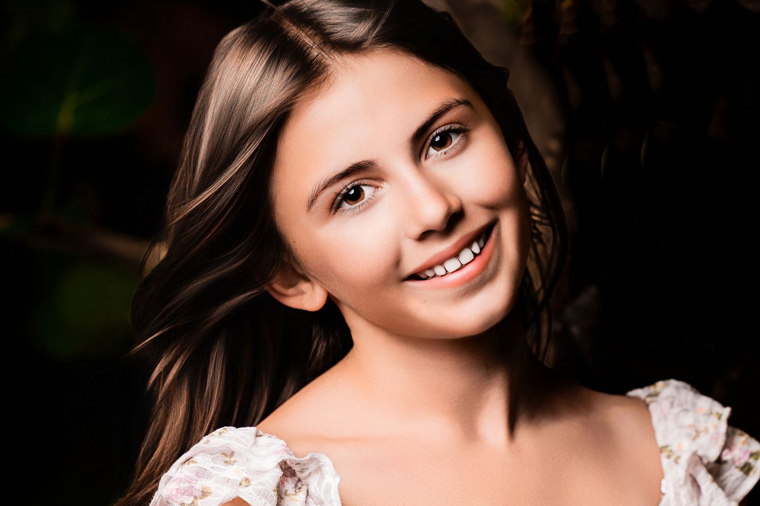 Smiling young woman with long brown hair posing for a close-up portrait outdoors