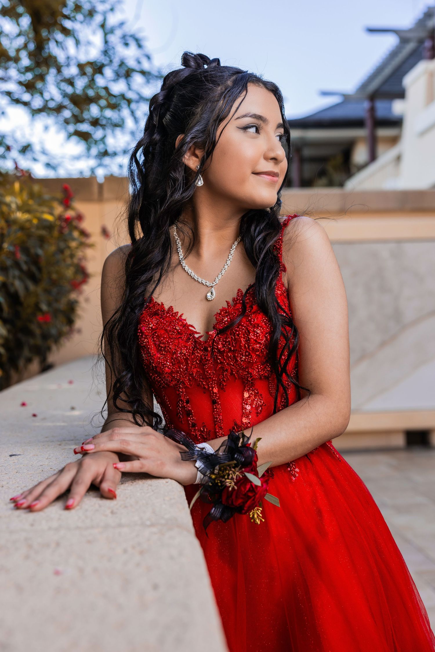 Young woman with long dark hair wearing an embellished red formal gown posing outdoors.