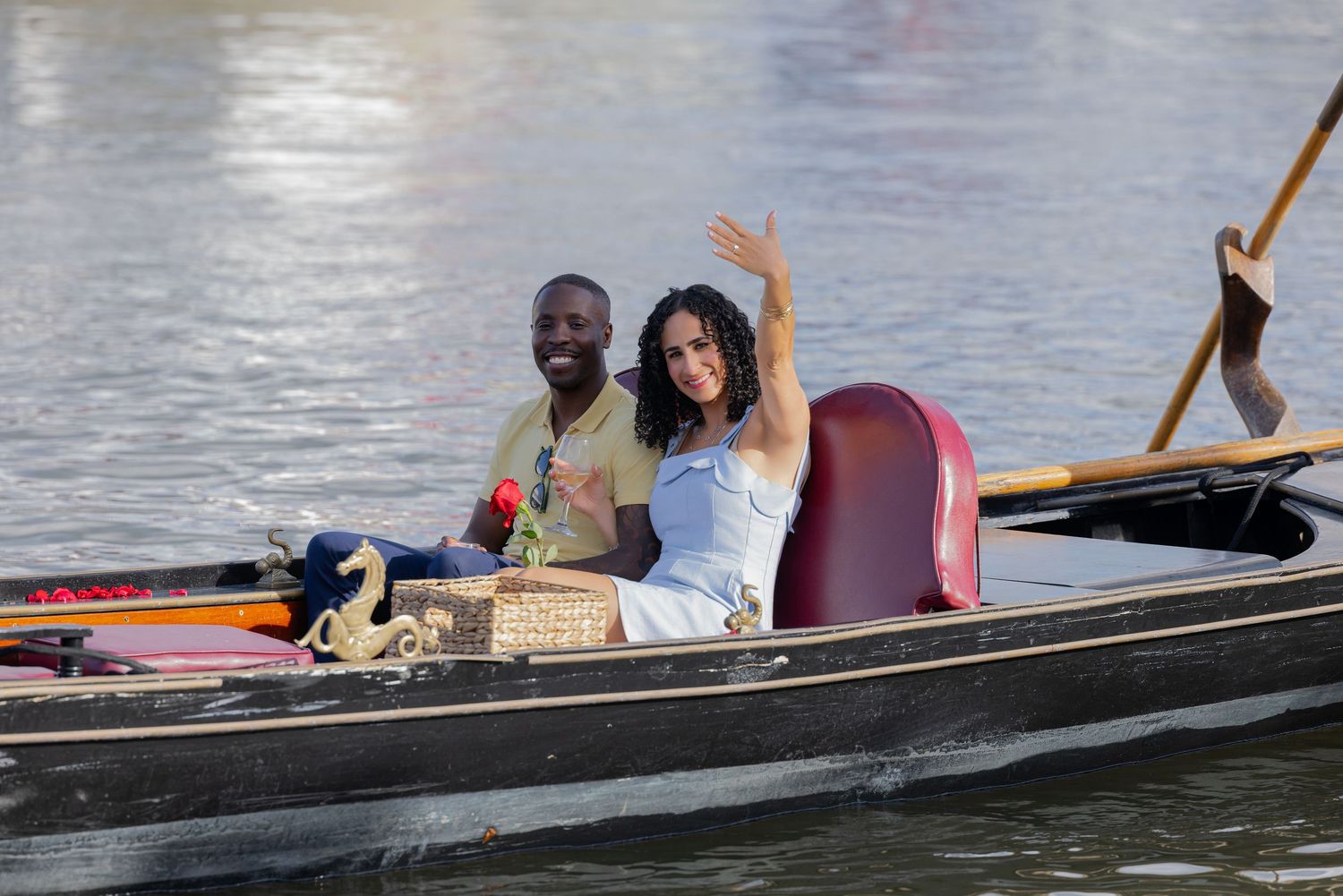Smiling couple waving while enjoying a scenic gondola boat ride on the water