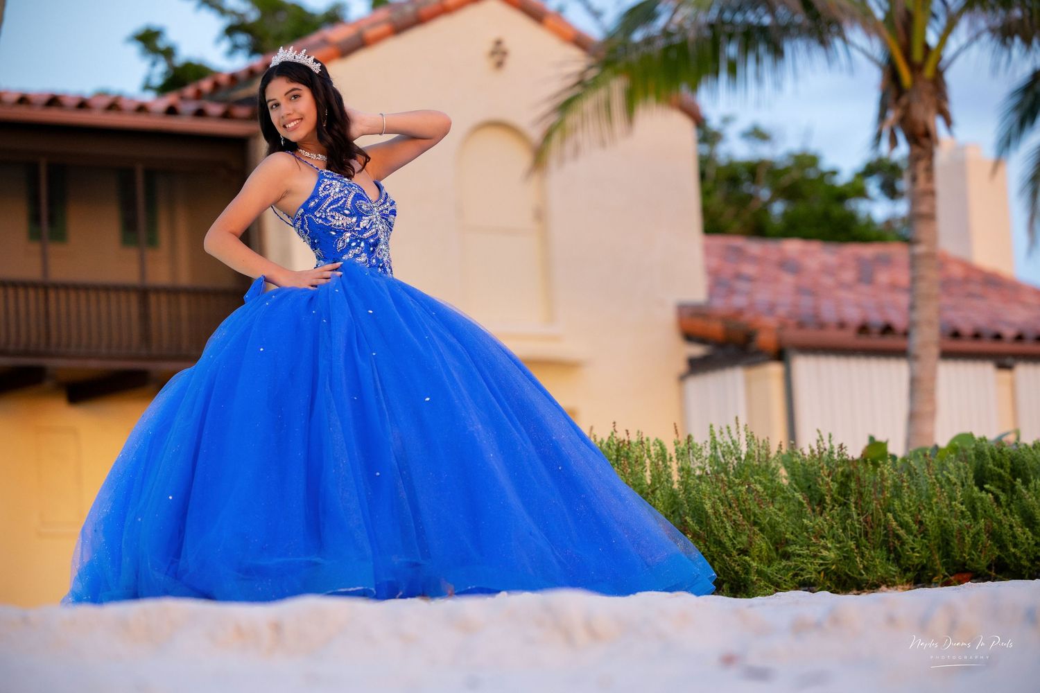 Glamour portrait of a woman in an embellished pink ruffled ballgown under outdoor string lights