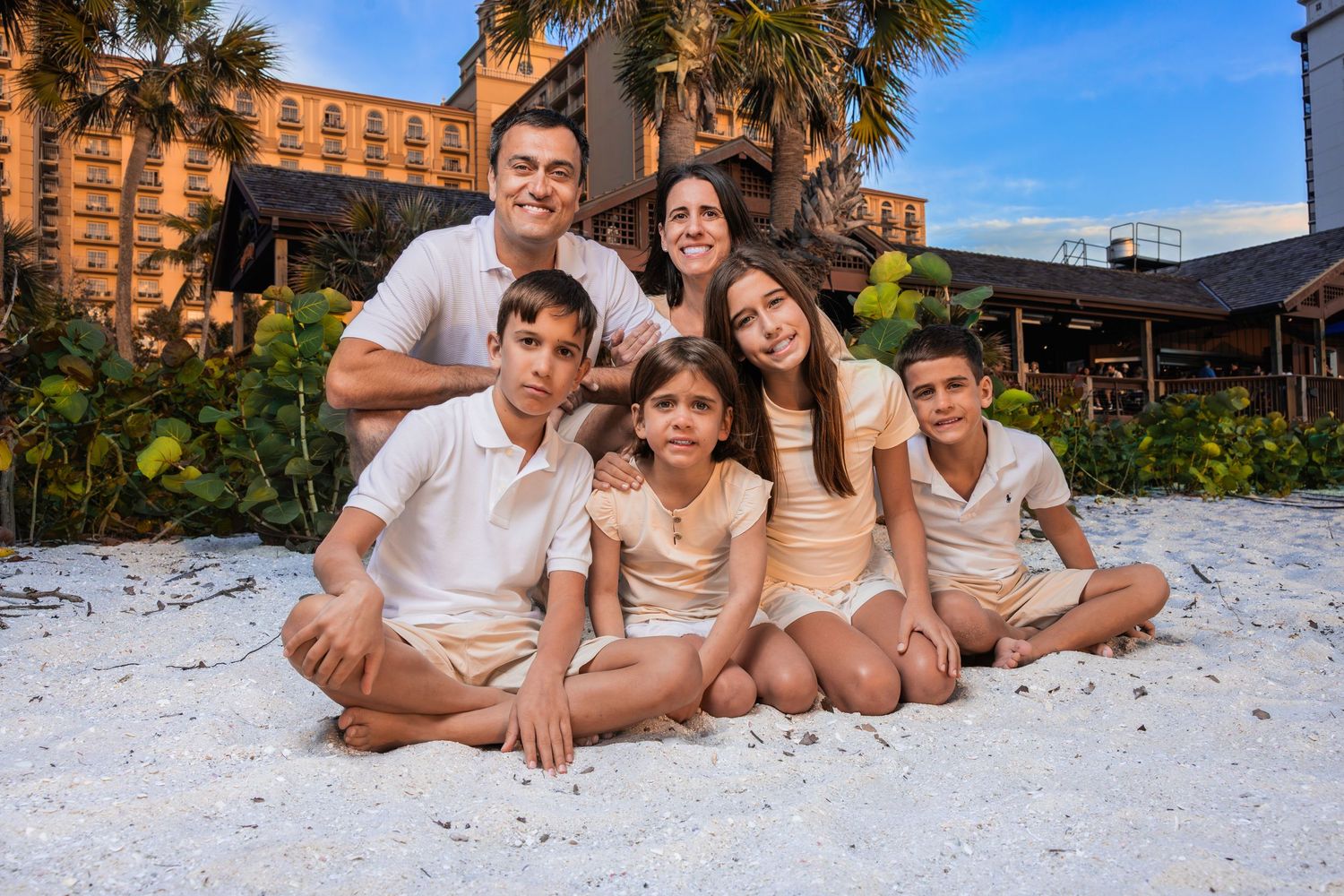 Family of five smiling and sitting together on a sandy white beach during a family vacation