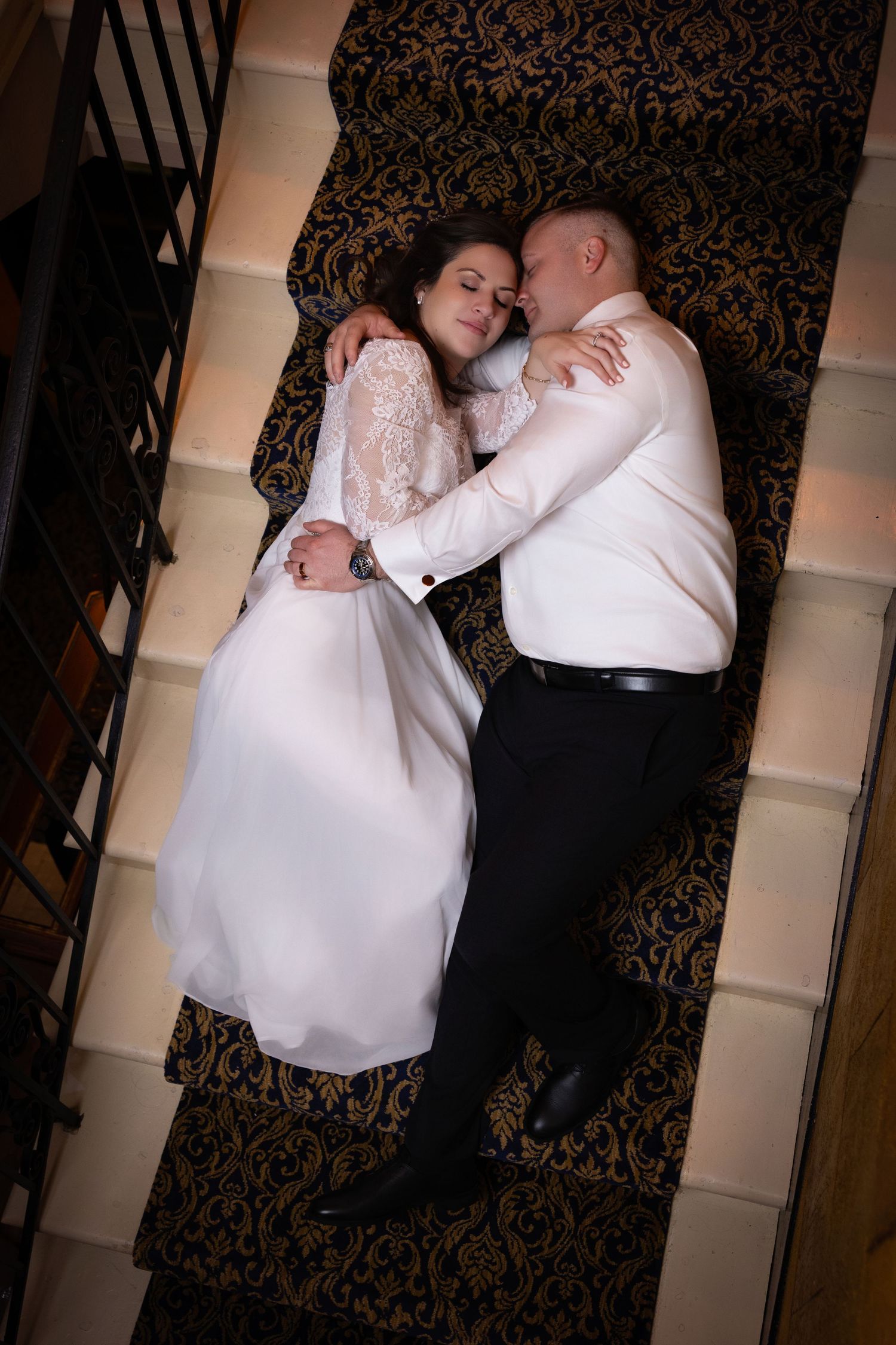Overhead view of a newlywed couple cuddling while lying down on a carpeted staircase