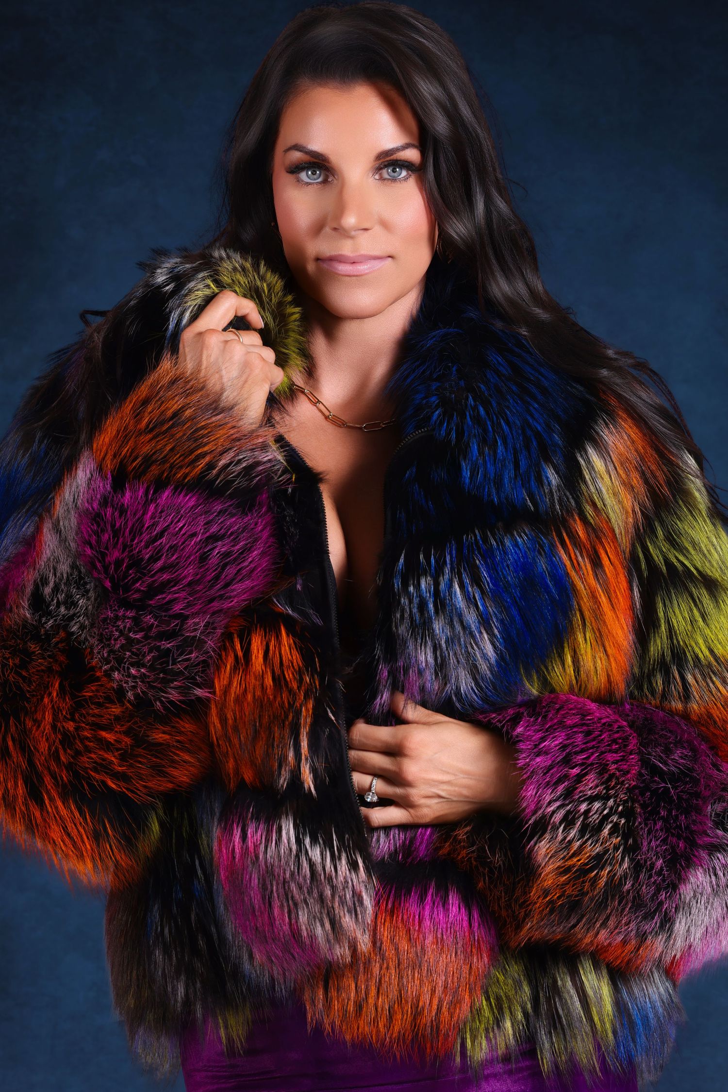 Studio portrait of a dark-haired woman modeling a vibrant, multi-colored patchwork textured fur jacket.