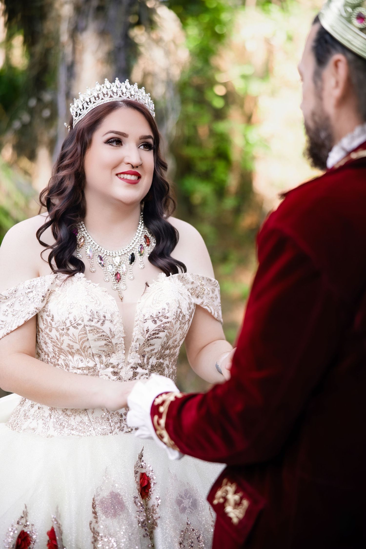 Bride in a beaded wedding gown and tiara holding hands with a groom wearing a red velvet royal coat