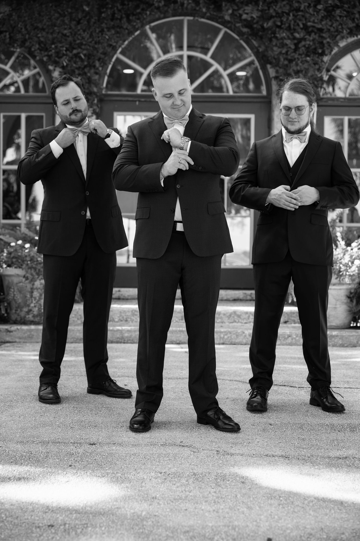 Black and white portrait of a groom standing in front of his groomsmen outside a wedding venue