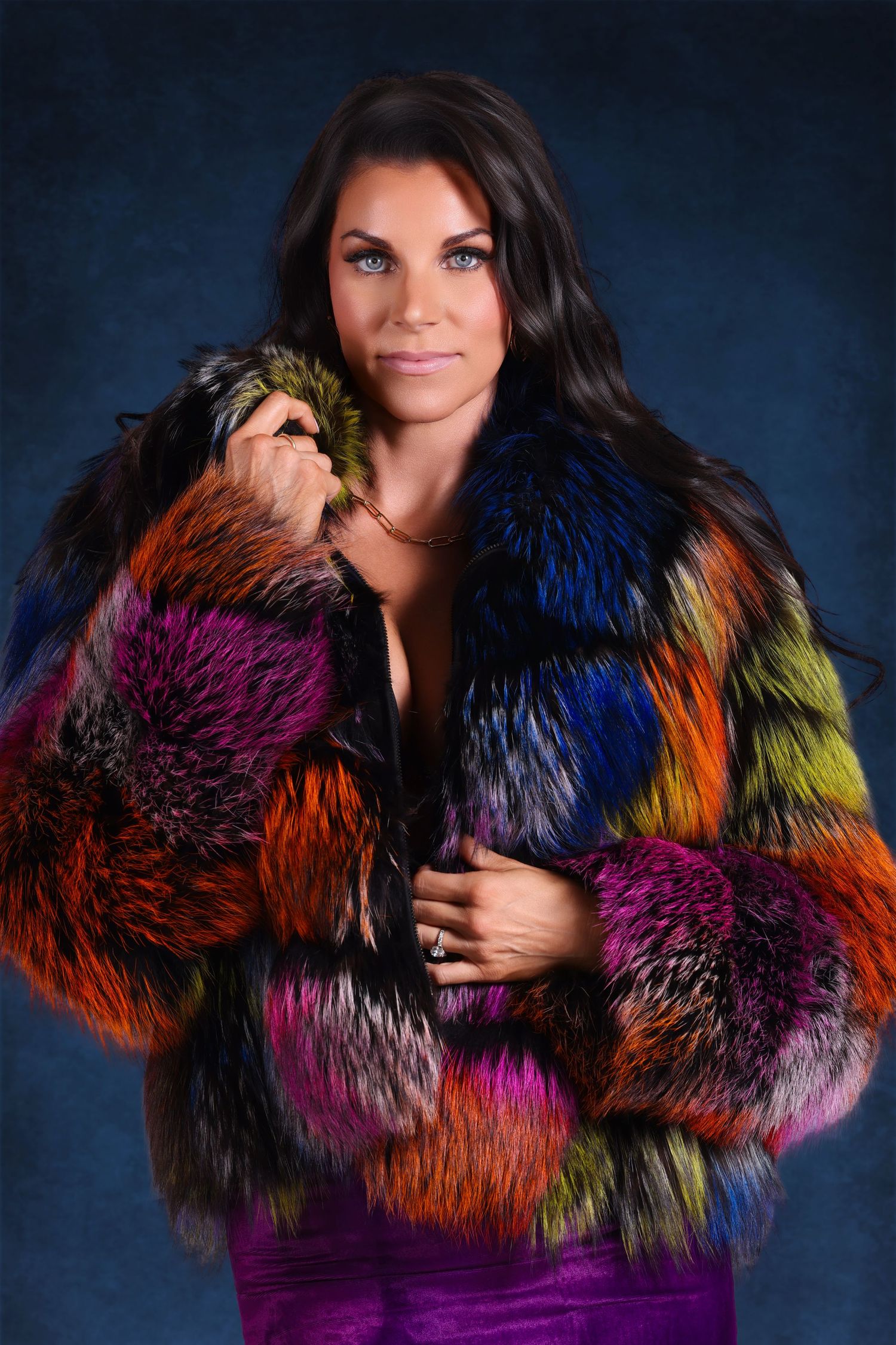 Studio portrait of a dark-haired woman modeling a vibrant, multi-colored patchwork textured fur jacket.