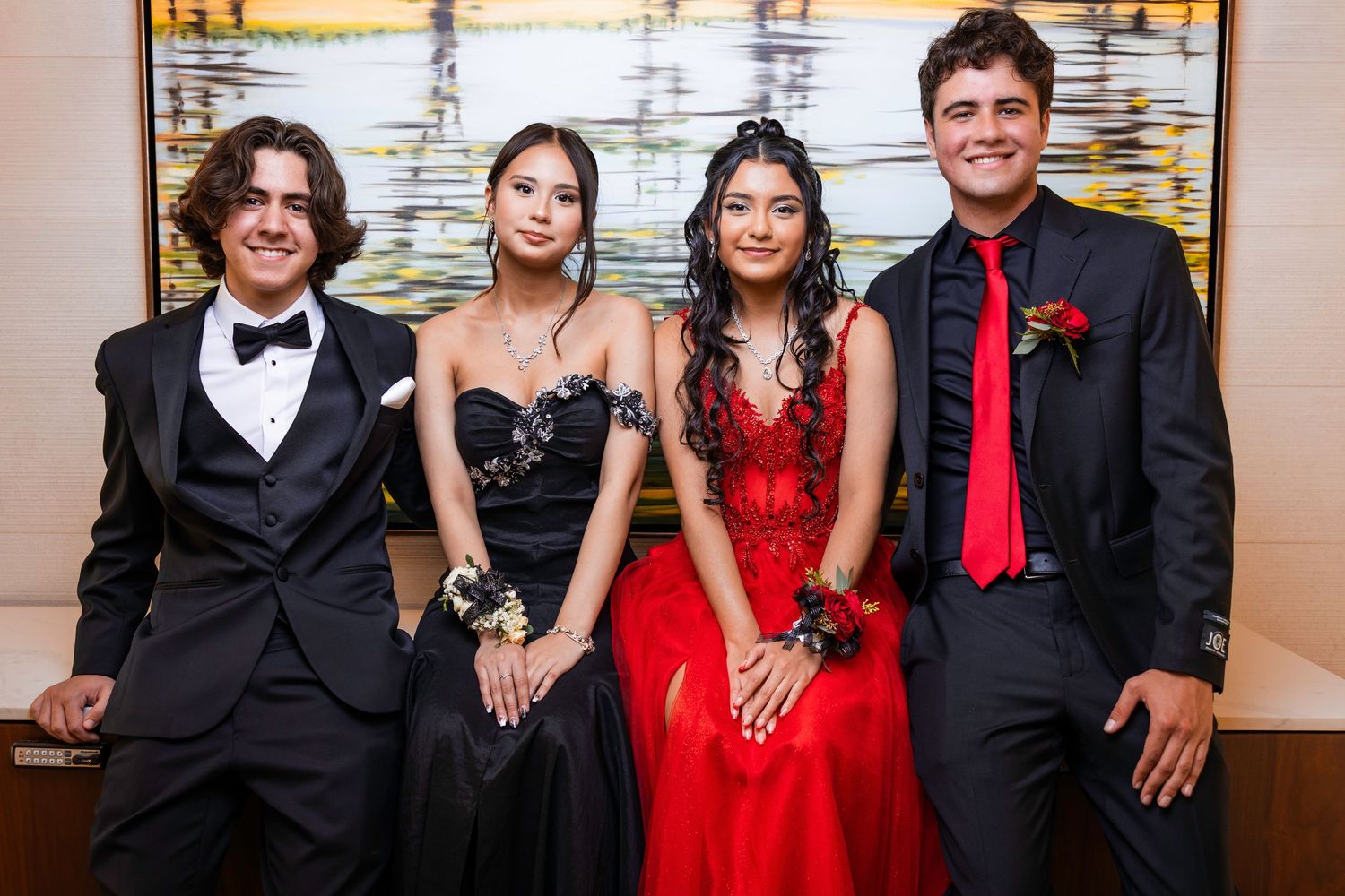 Two couples posing together indoors wearing elegant black and red formal prom attire