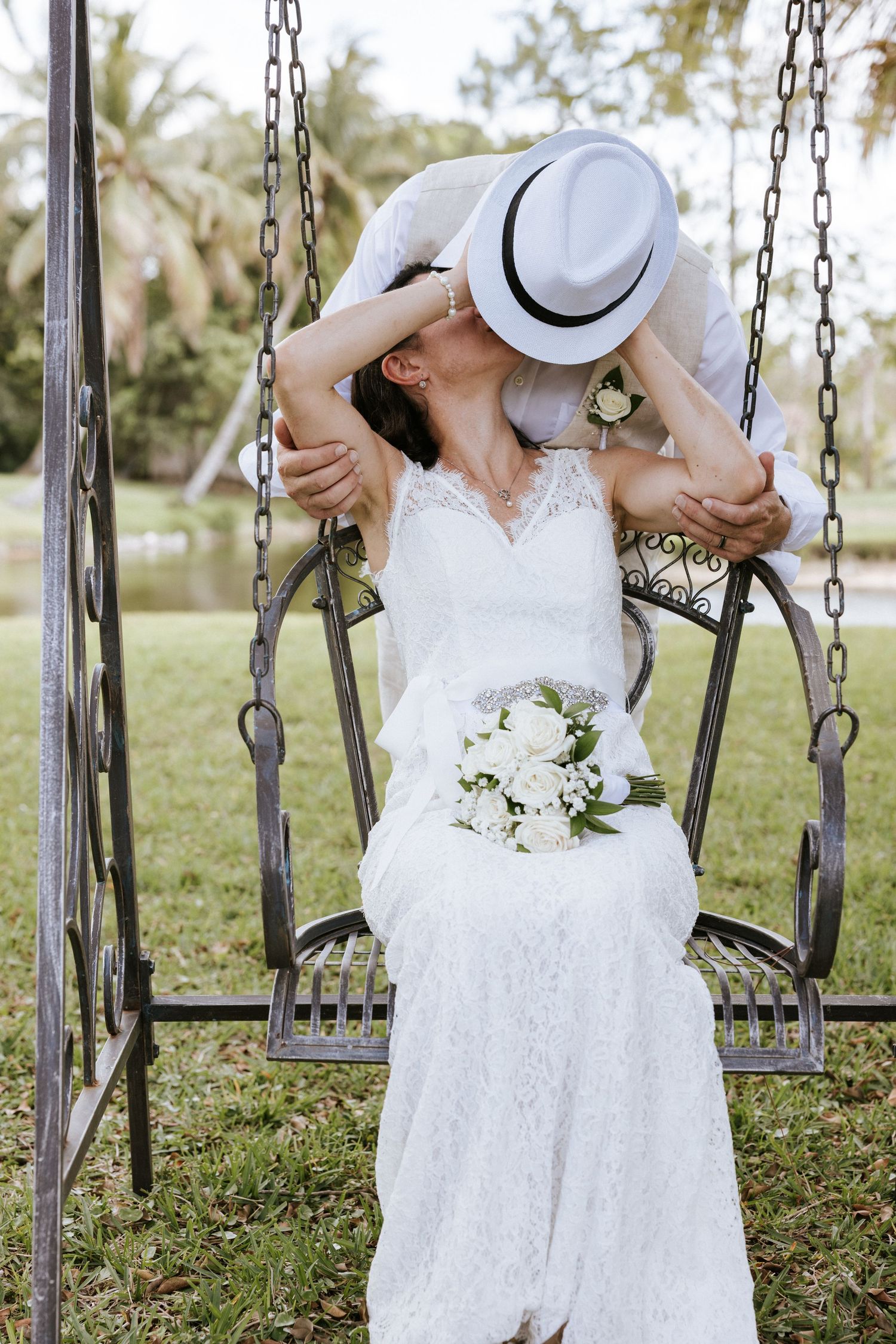 Groom leaning down to kiss a bride sitting on a metal garden swing on her wedding day