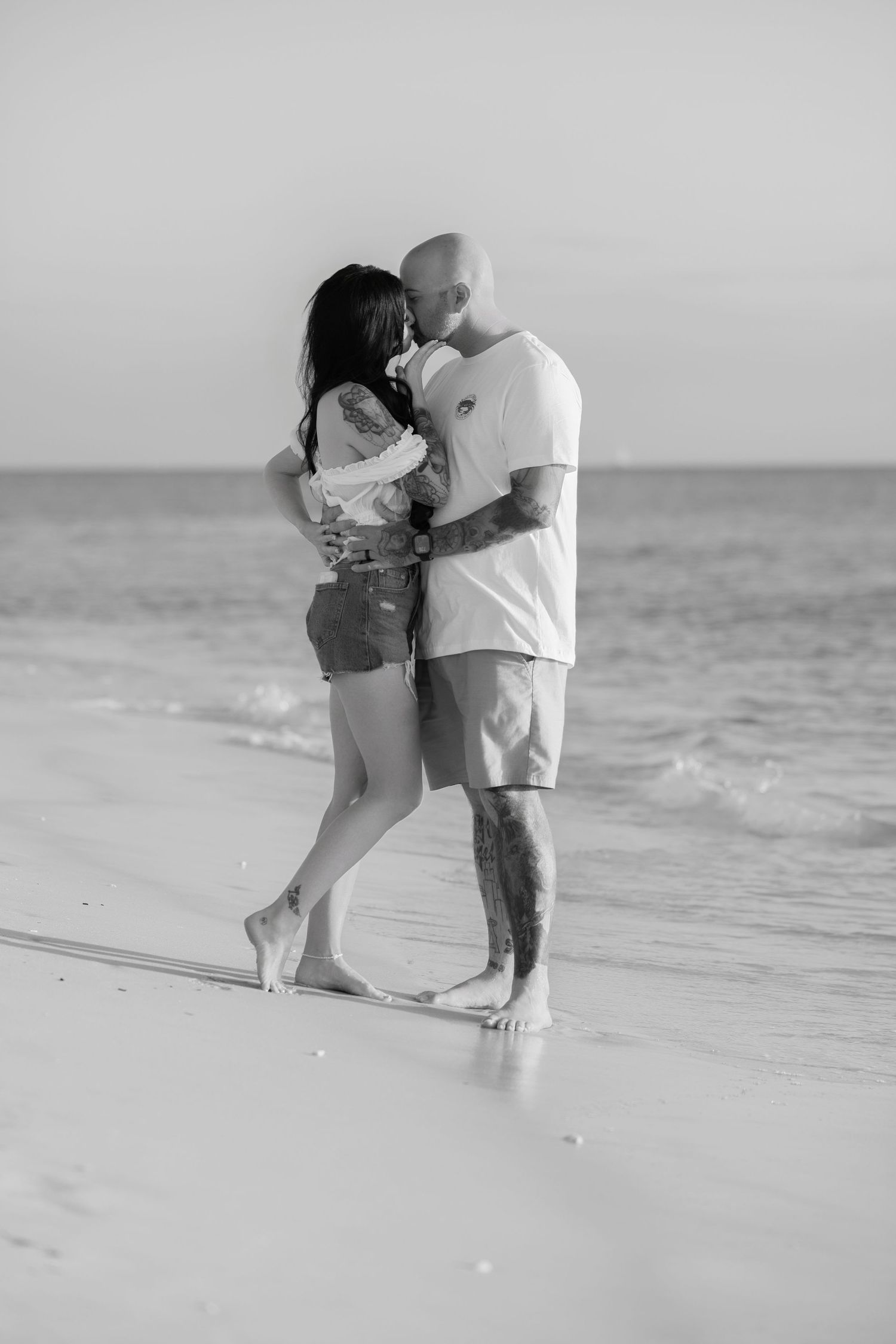 Black and white photo of a couple hugging barefoot on a sandy beach shore
