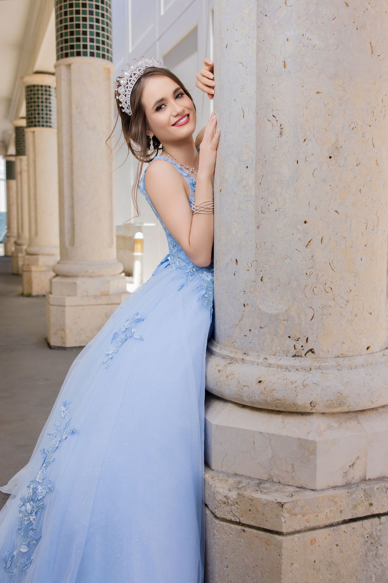 Young woman wearing a light blue strapless formal dress leaning against an architectural stone pillar