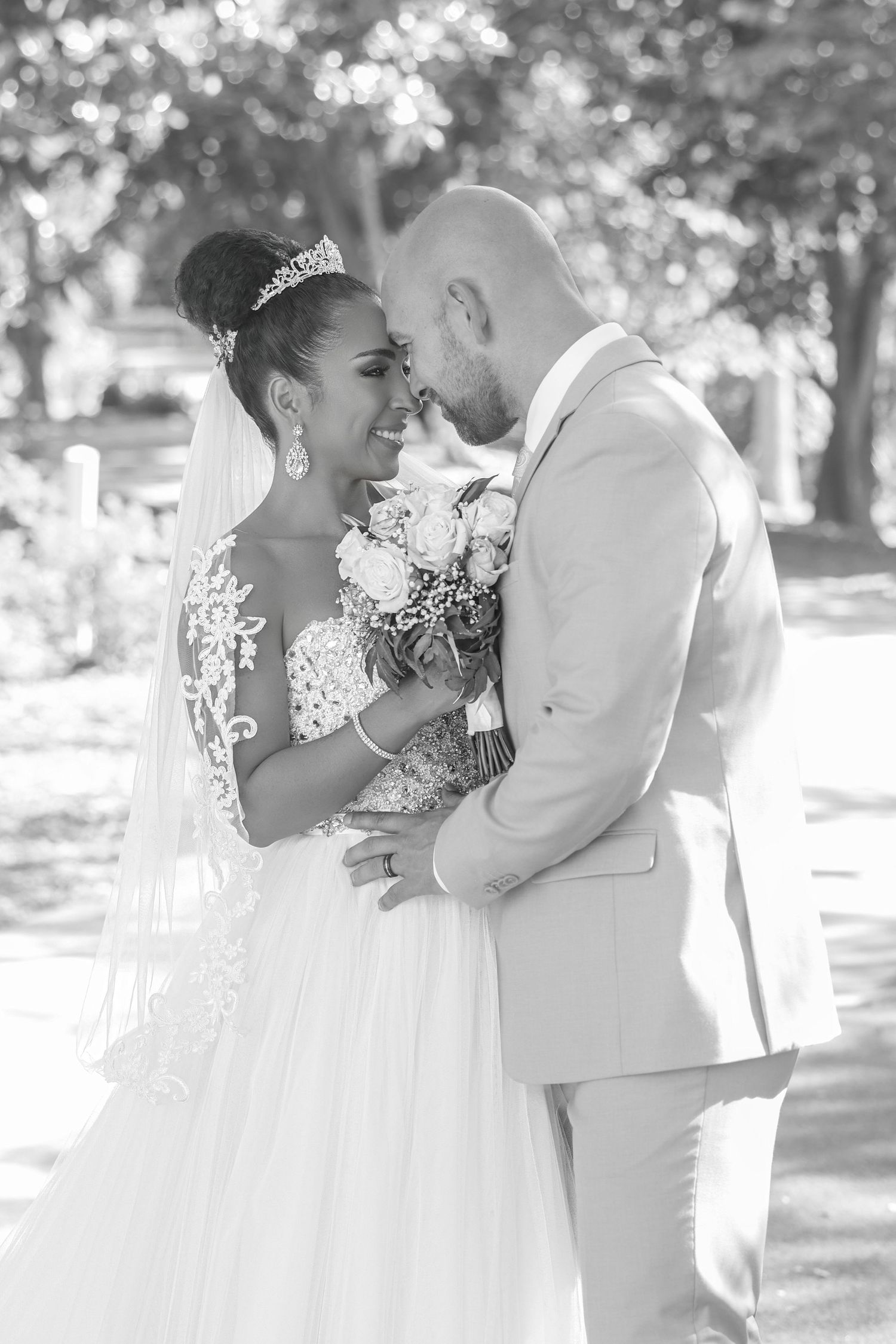 Black and white photo of a newlywed bride and groom smiling at each other in a sunny garden setting
