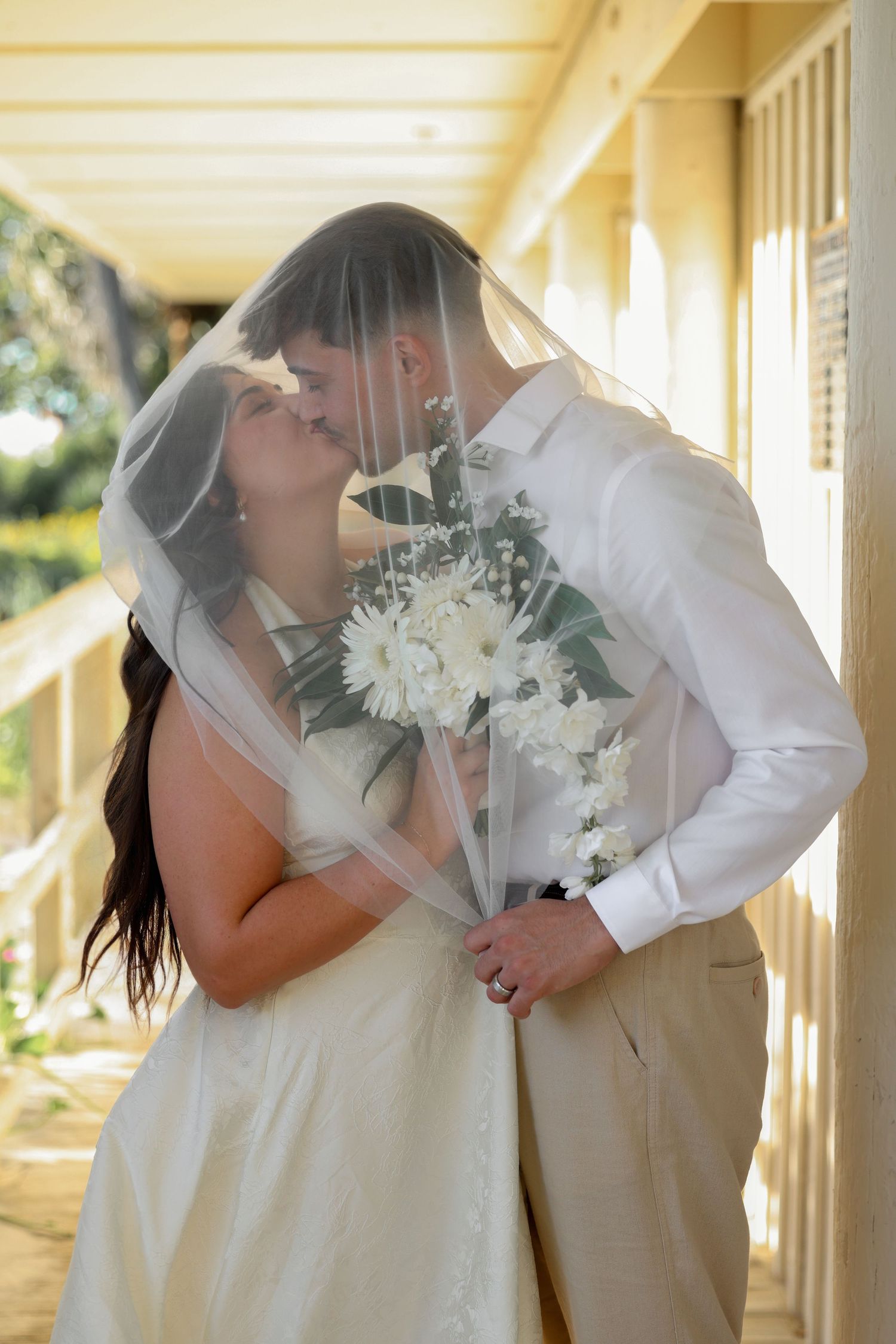 Wedding couple kissing behind the flowing fabric or veil of the bride’s wedding dress.
