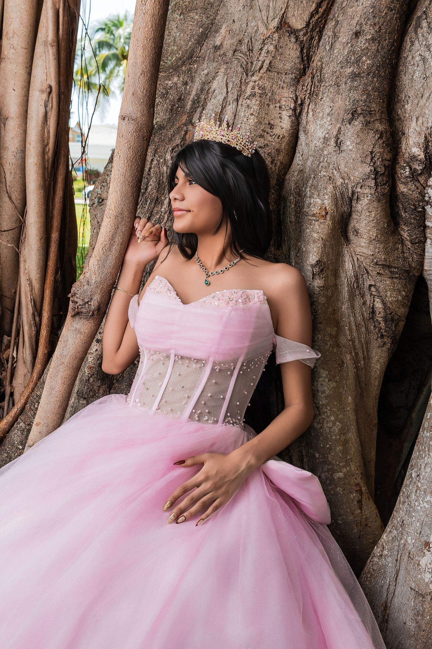 Young woman in a pink off-the-shoulder ballgown posing next to a large banyan tree root