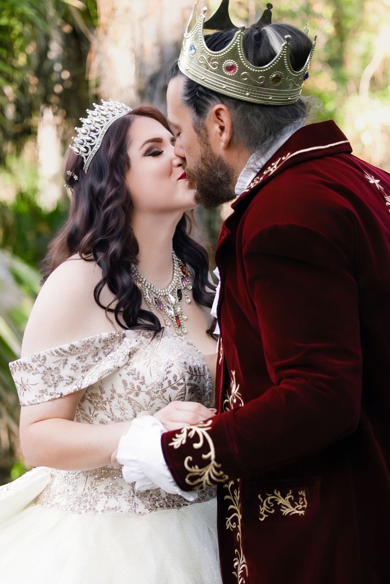 Groom wearing a royal crown and red velvet coat kissing his bride on the forehead during a themed wedding
