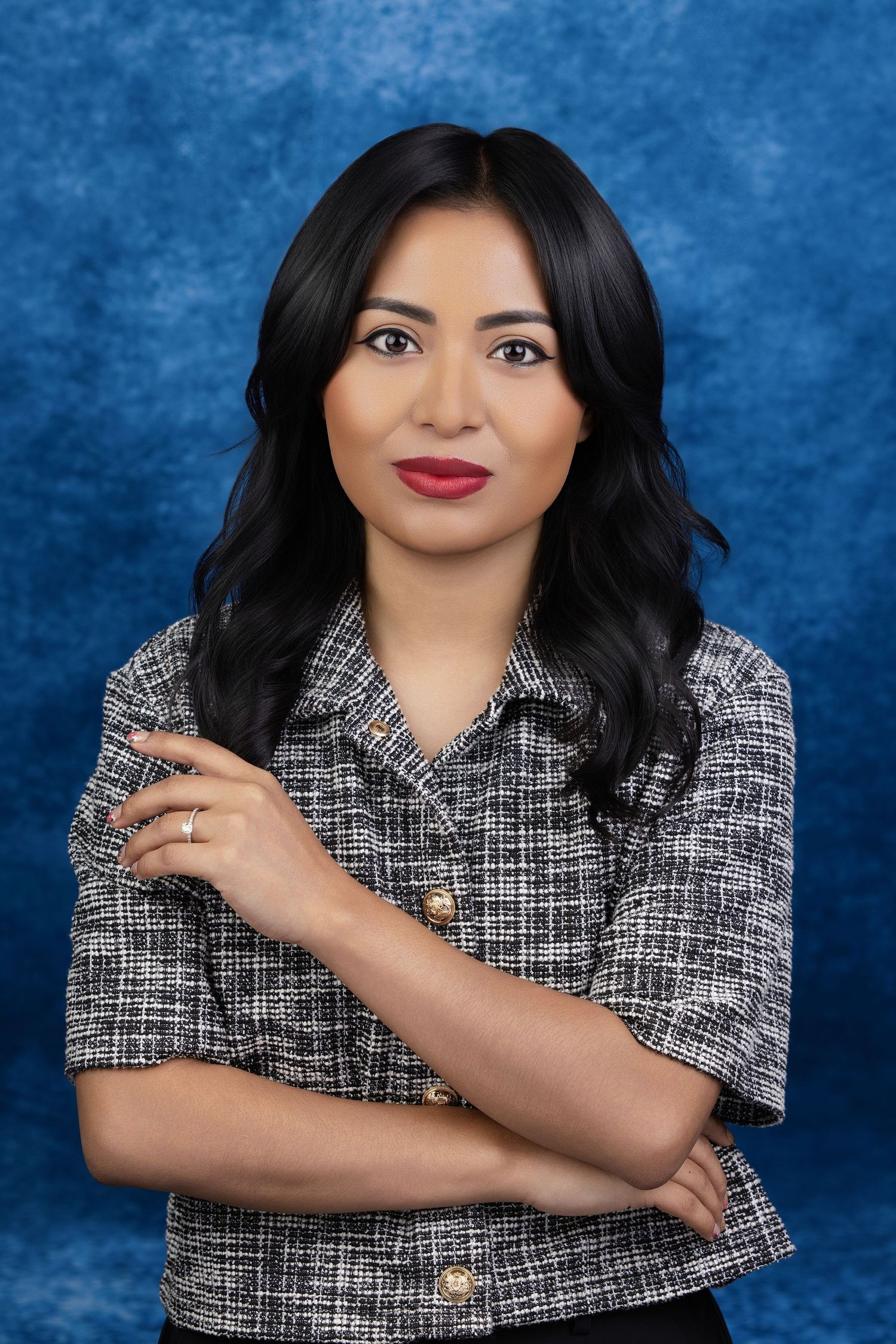 Smiling woman with dark hair posing with her arms crossed against a textured blue backdrop