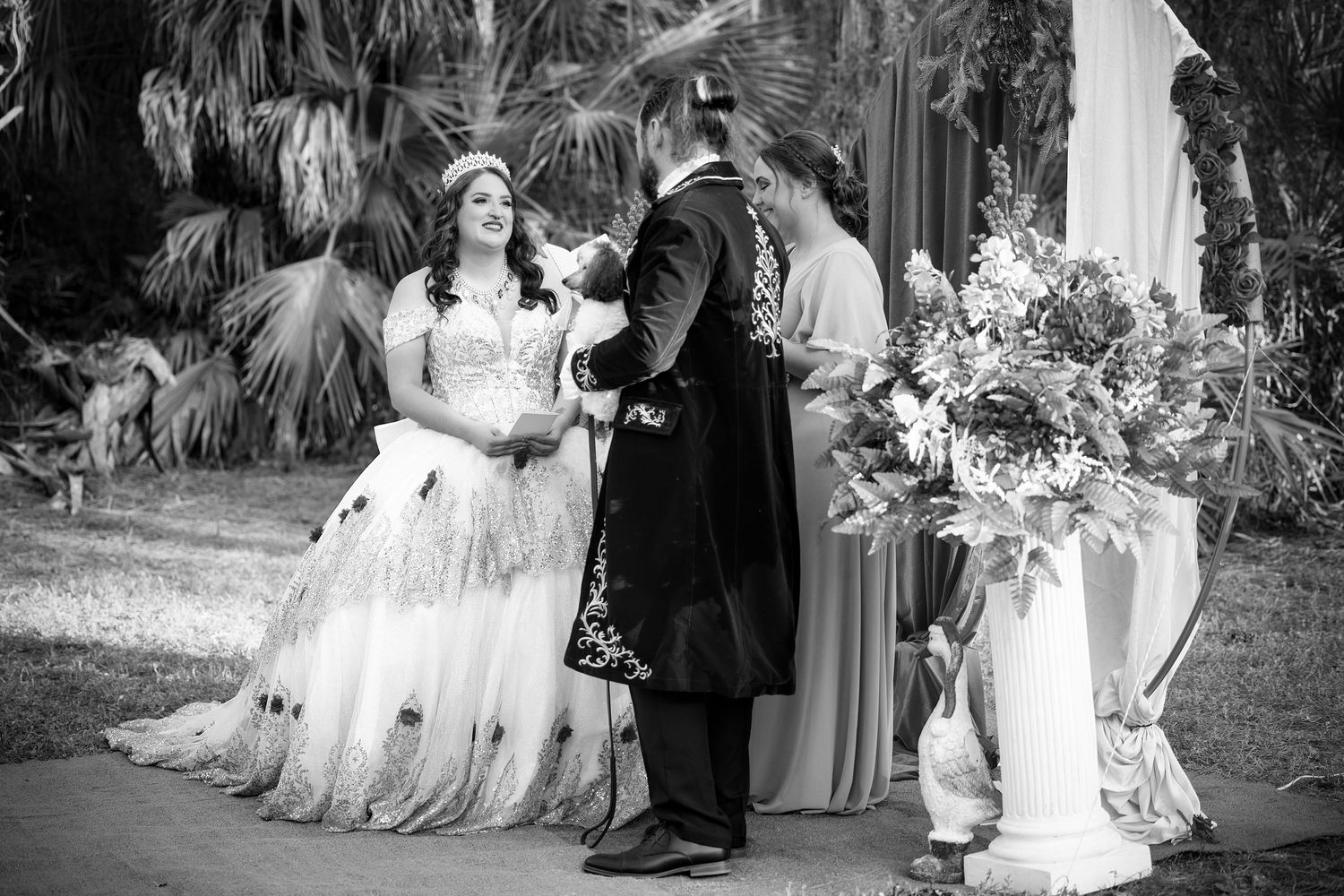 Black and white photo of a bride and groom holding hands during an outdoor backyard wedding ceremony
