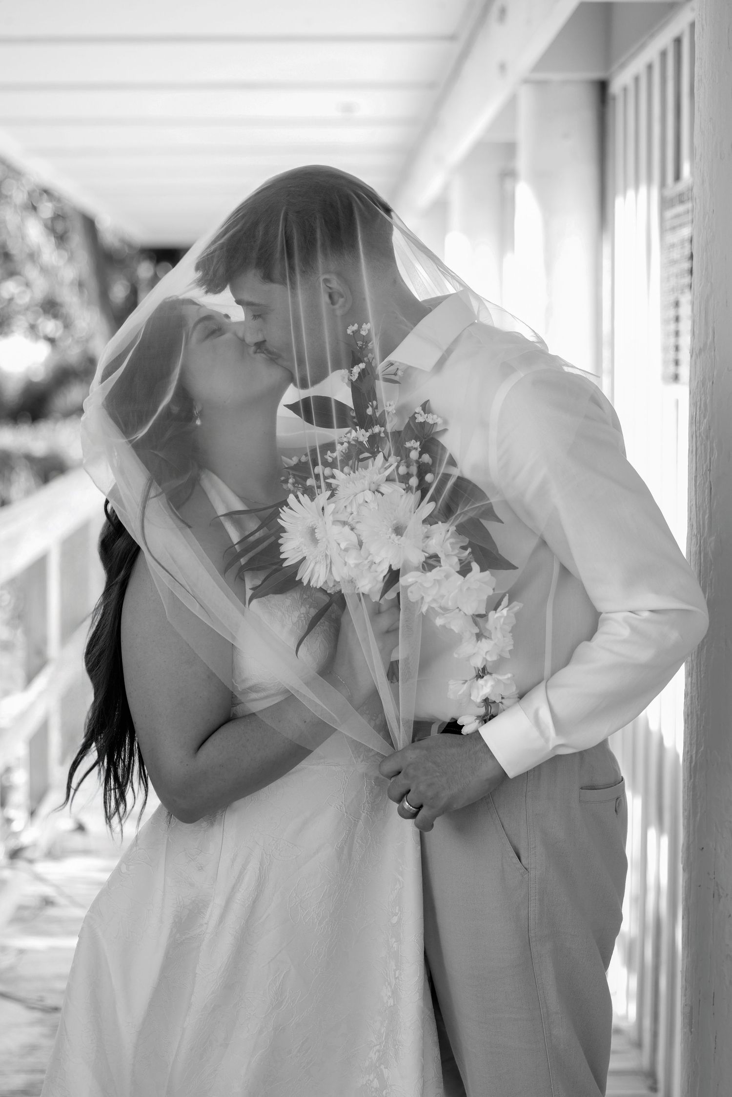Black and white portrait of a bride and groom embracing on an outdoor covered walkway