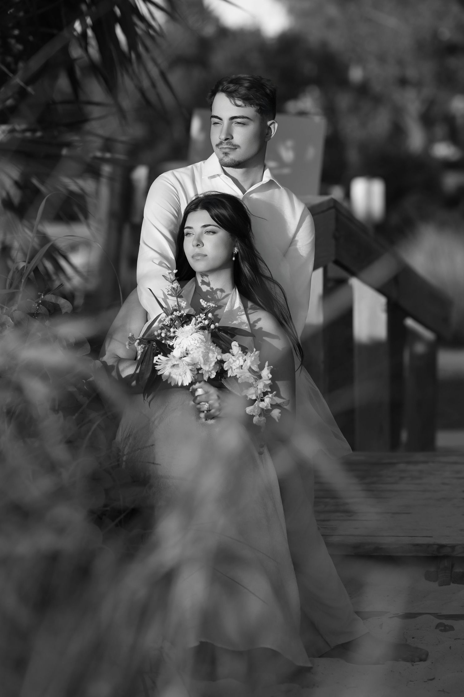 Black and white portrait of a groom embracing his bride from behind on a wooden garden bridge