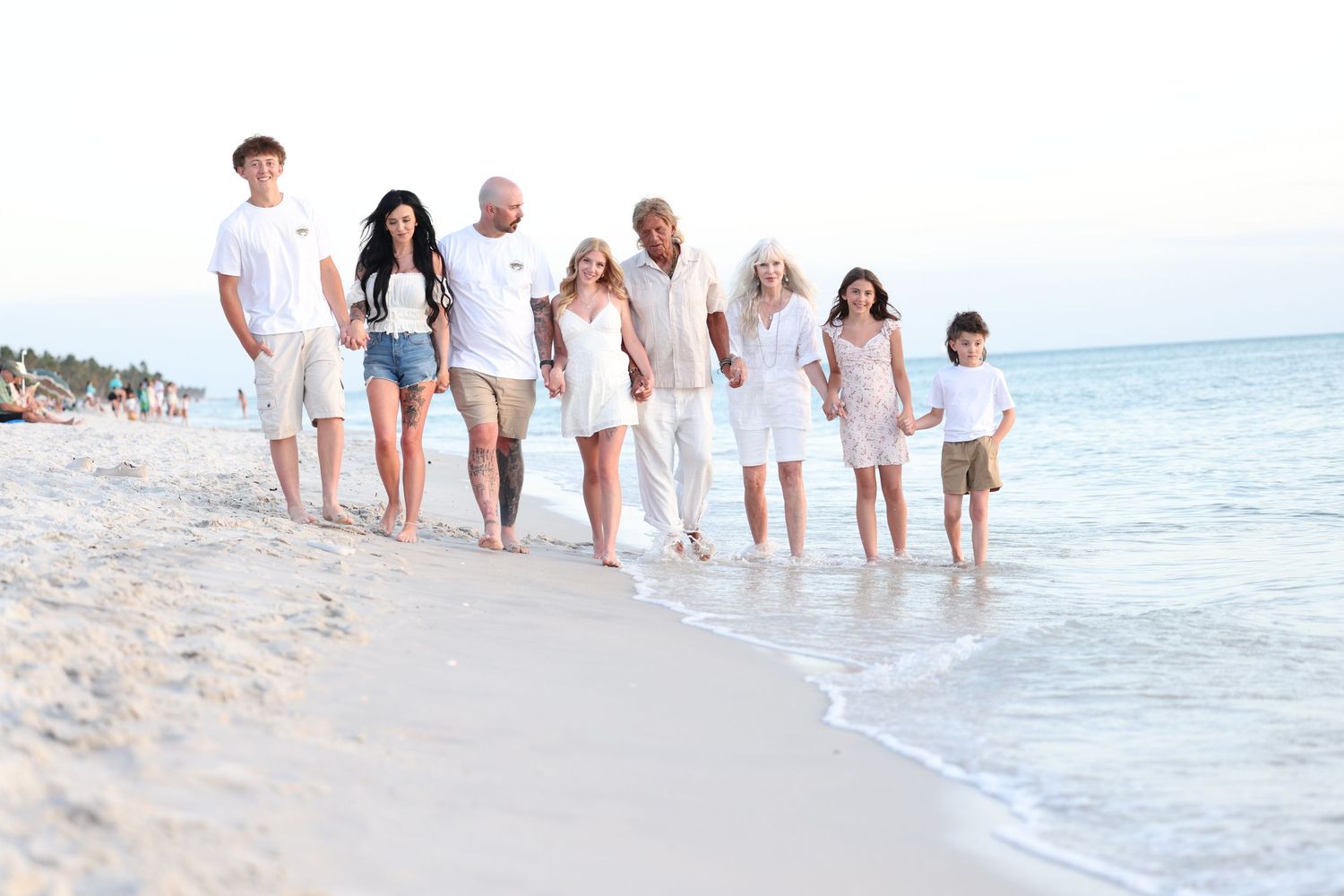 Large multi-generational family walking hand-in-hand along the ocean shoreline on a beach