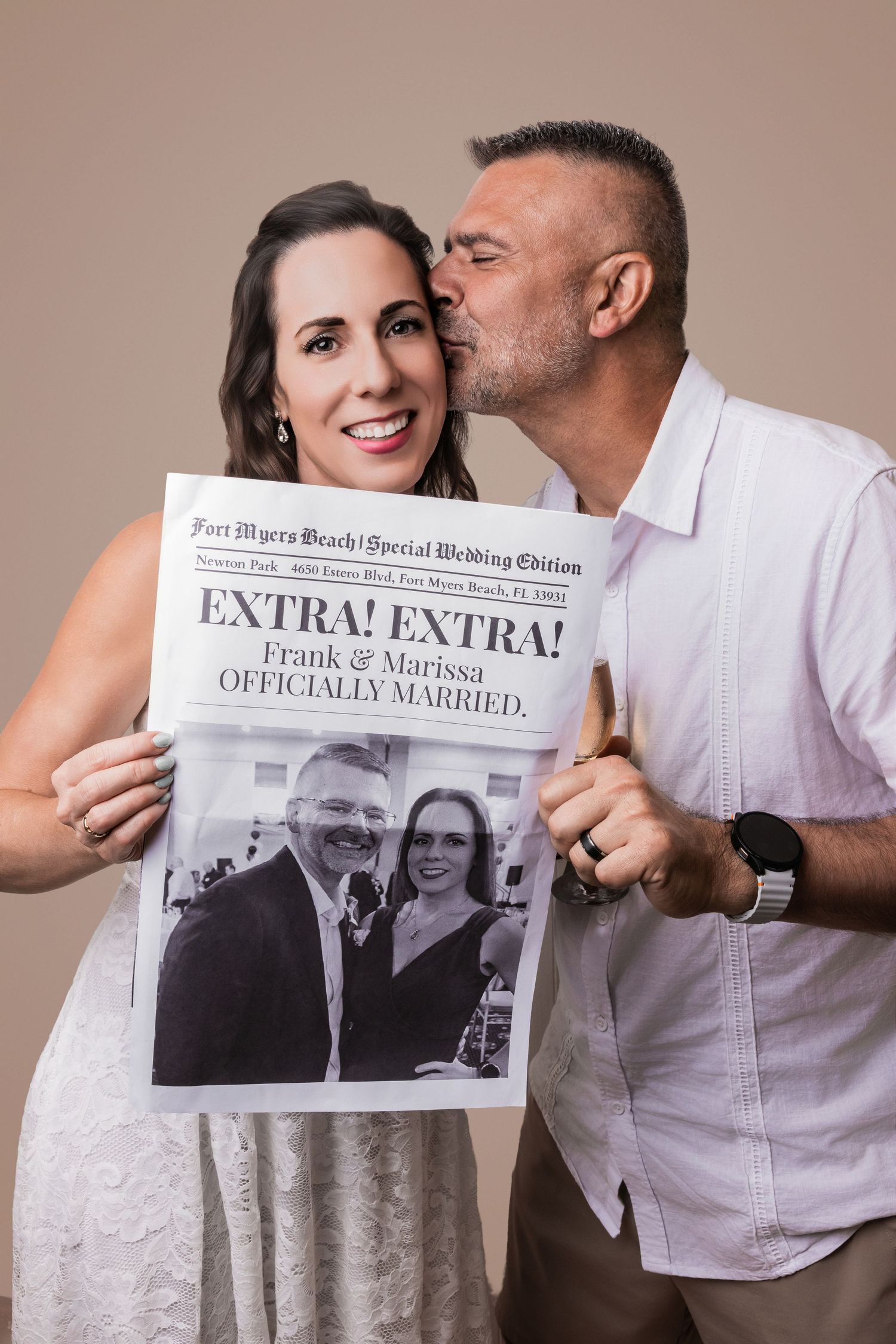 Man kissing a smiling woman on the cheek while she holds up a custom newspaper wedding announcement.