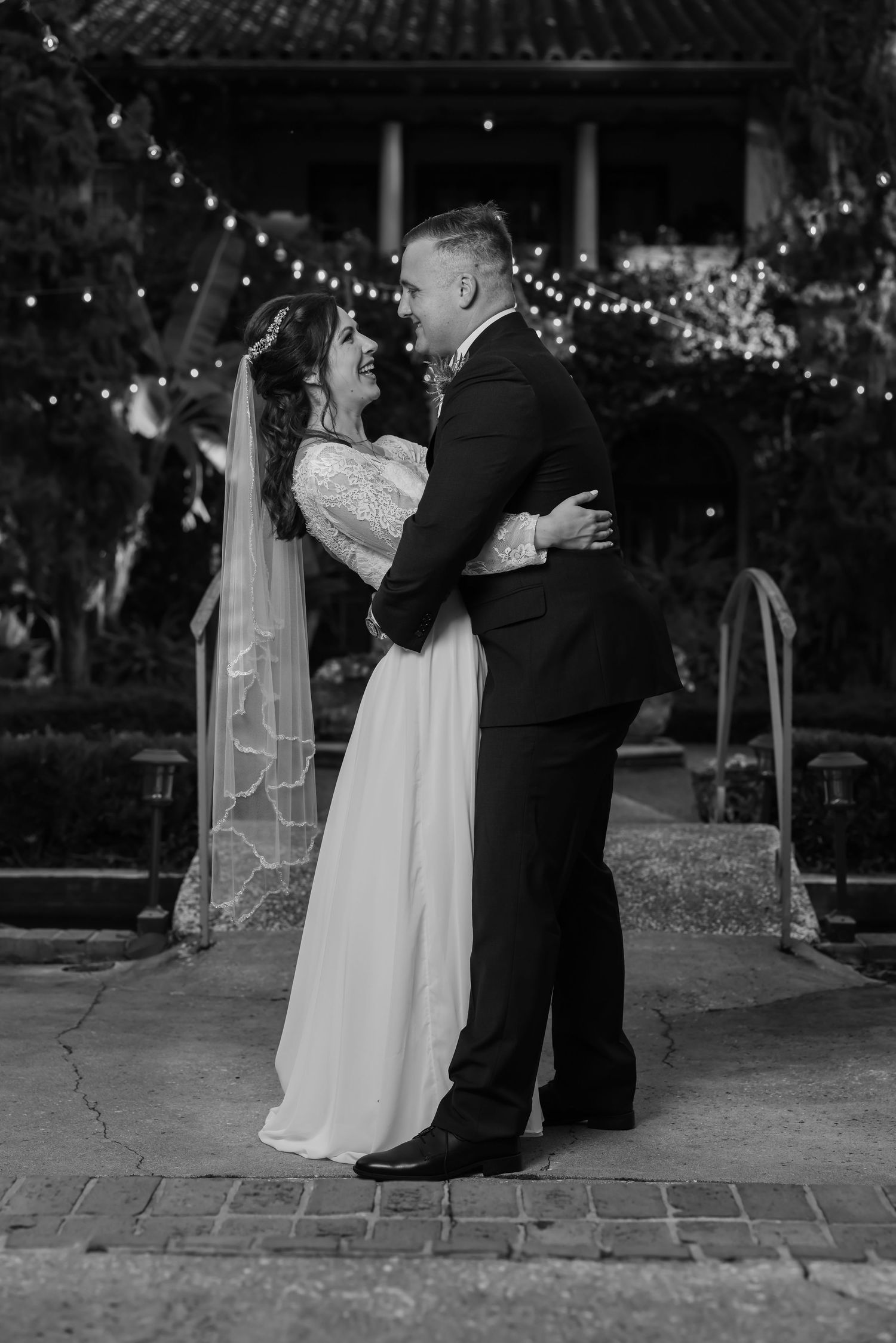 Black and white outdoor portrait of a couple kissing face-to-face under garden string lights