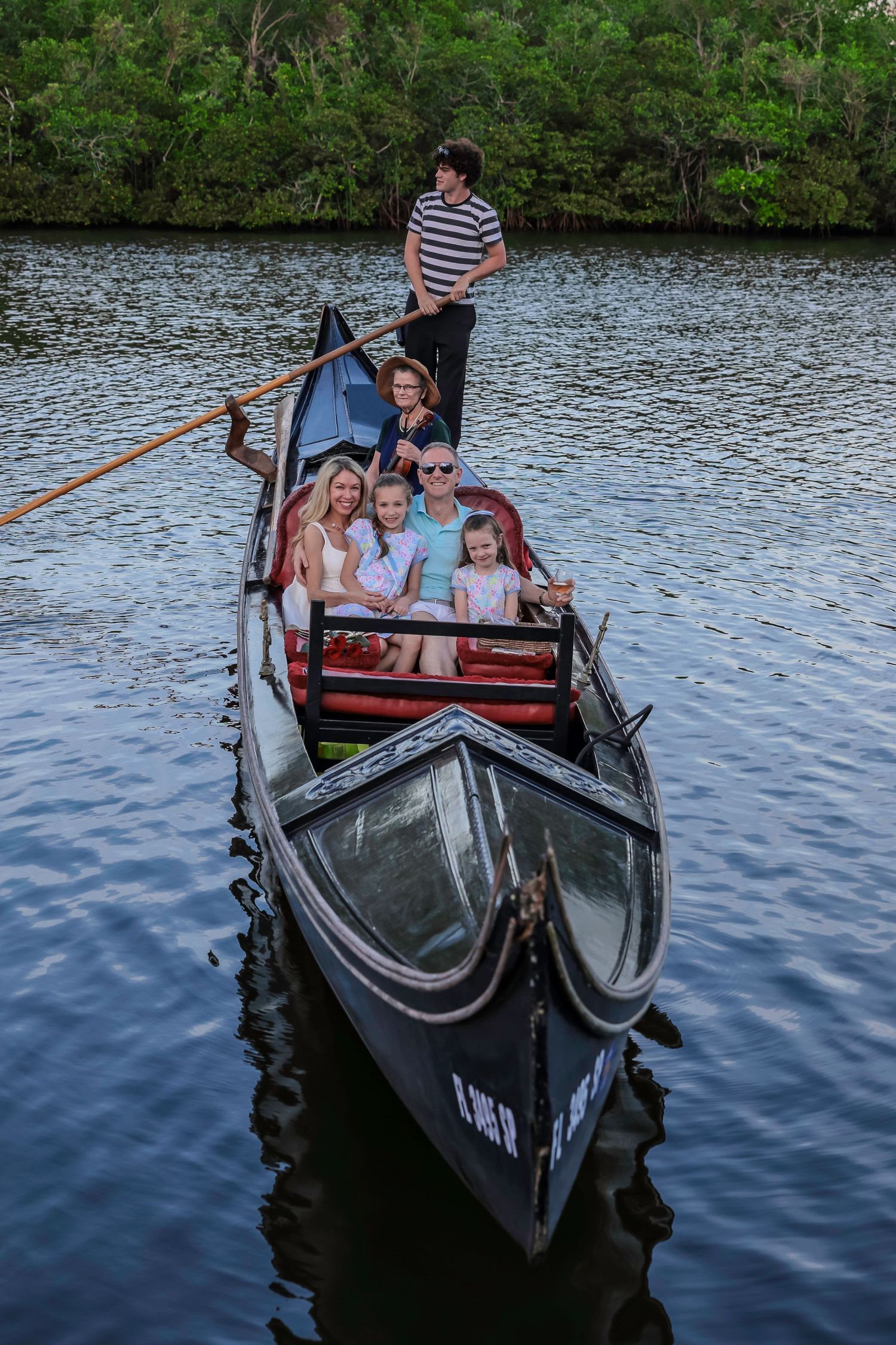 High-angle view of a gondolier steering a traditional black gondola boat with passengers down a canal