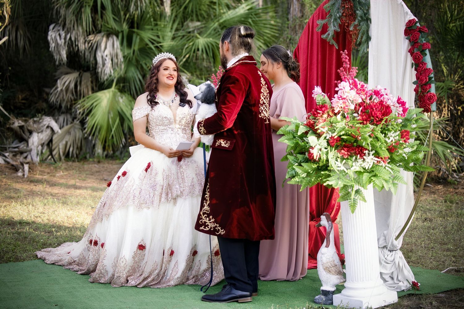 Bride and groom exchanging vows at an outdoor altar decorated with large red and white floral arrangements